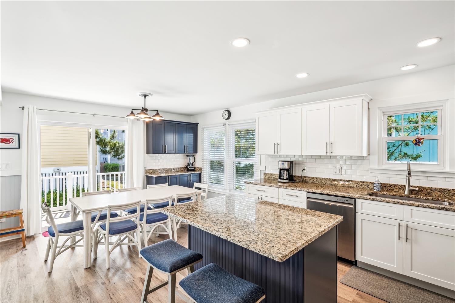 Step into your sunlit coastal kitchen where granite counters, stainless appliances, and an inviting island await your culinary adventures, with glimpses of turquoise waters through the windows.