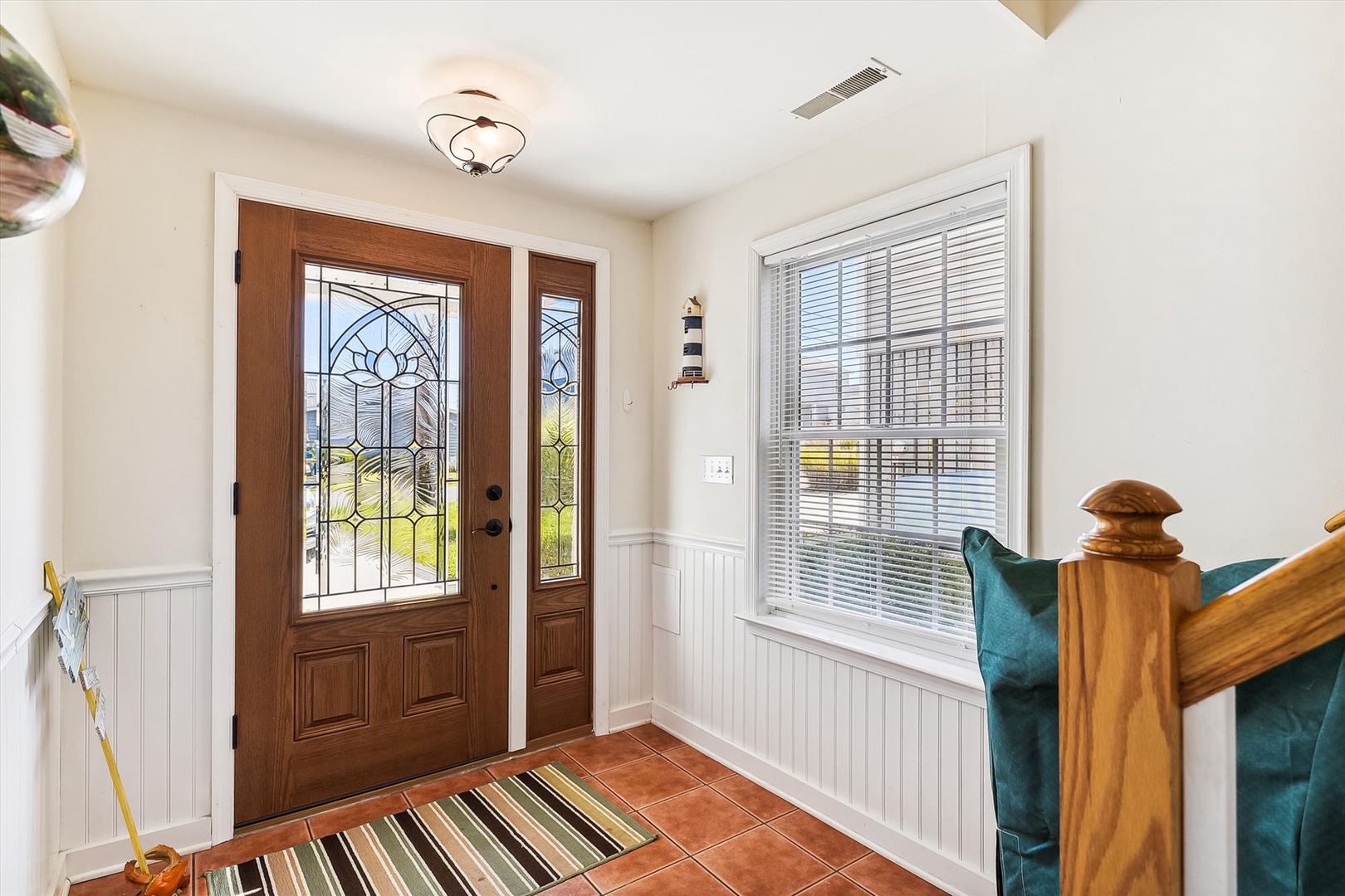 Step inside to a bright, welcoming entryway with elegant wood doors and warm natural light streaming through stained glass and large windows.