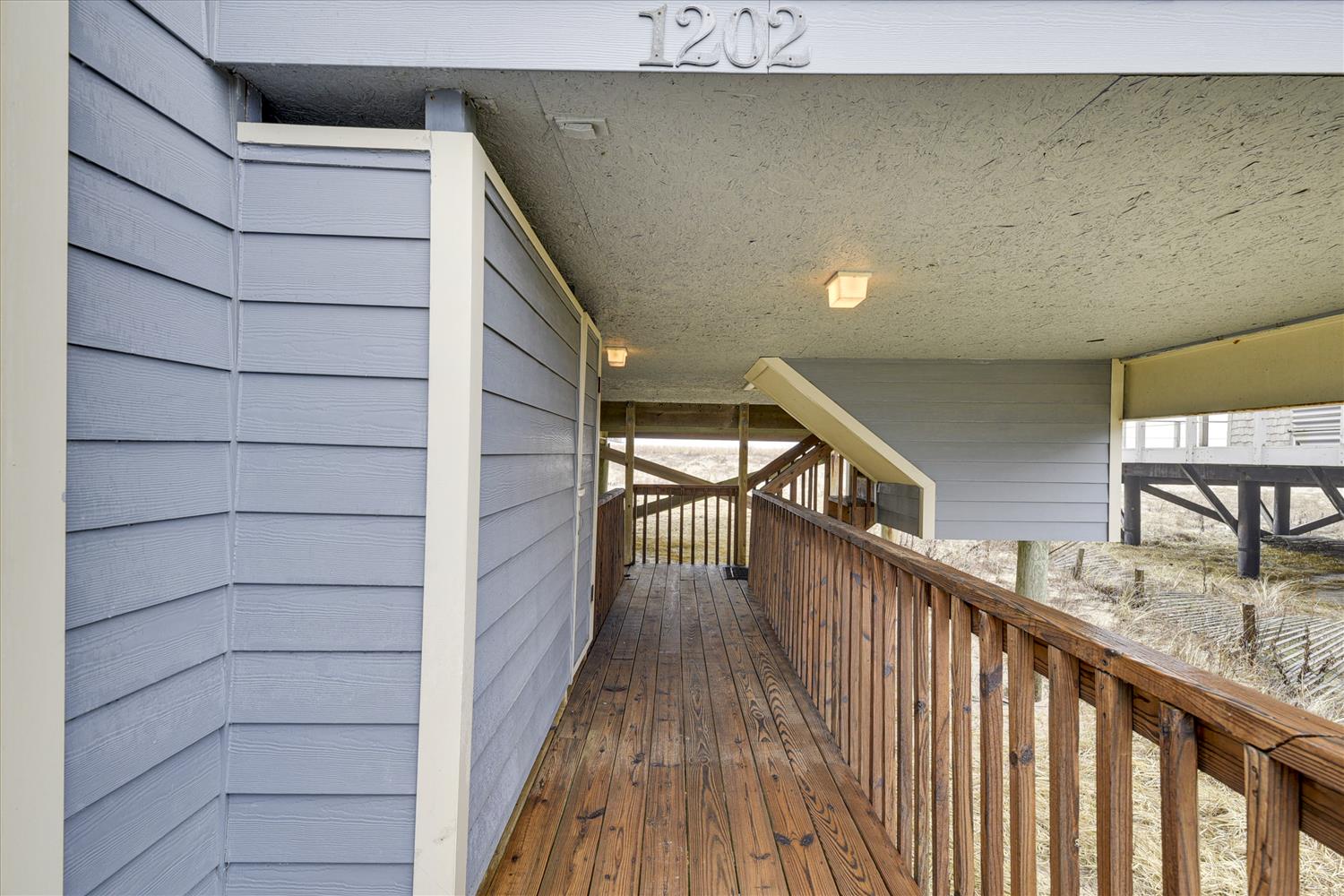 Unit 1202 welcomes you via a private covered walkway with natural wood railings and coastal surroundings visible beyond.