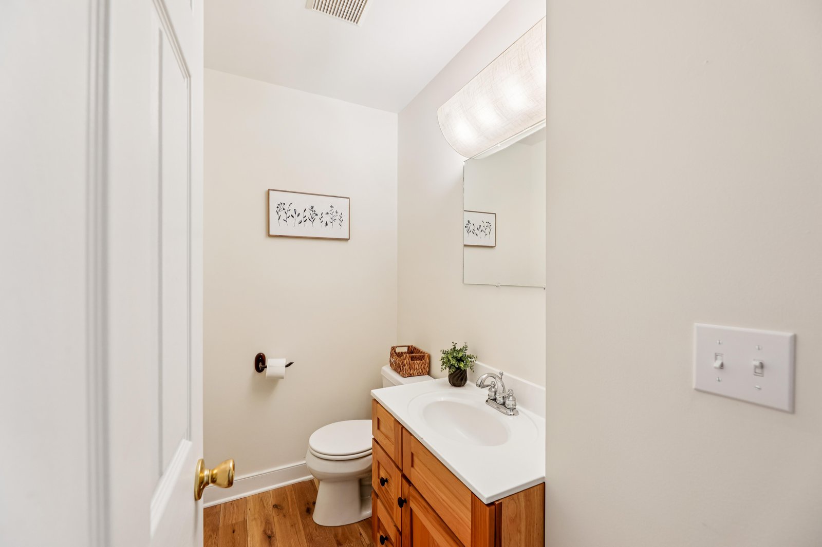 Step into a bright, freshly updated bathroom with warm wood vanity, clean white counters, and charming botanical artwork that creates a calm, welcoming space for your daily routine.