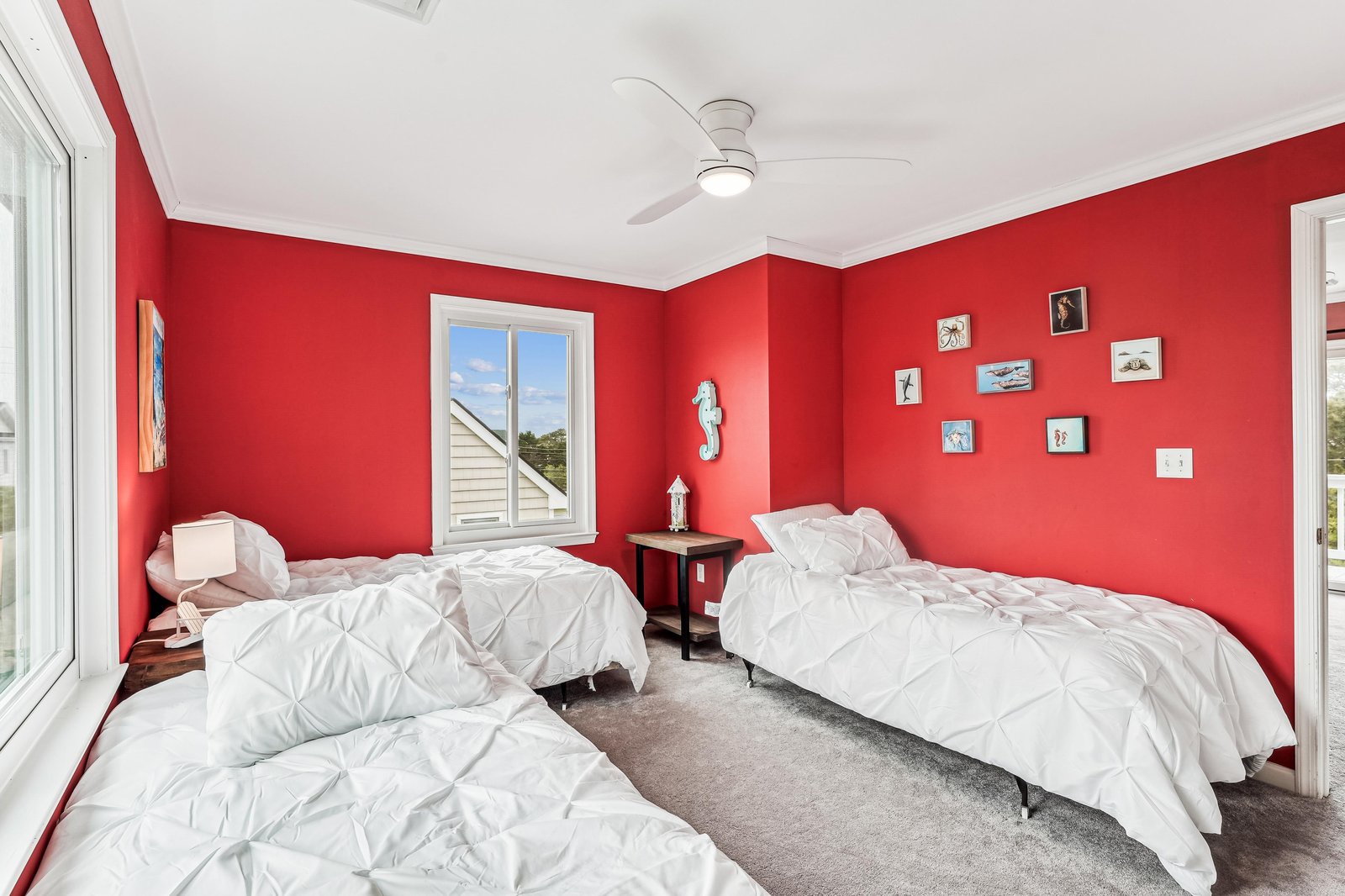 Vibrant coral walls wrap around your space, where three plush beds promise restful nights. A ceiling fan keeps you cool while coastal art and cheerful accents set a playful, beachy mood.
