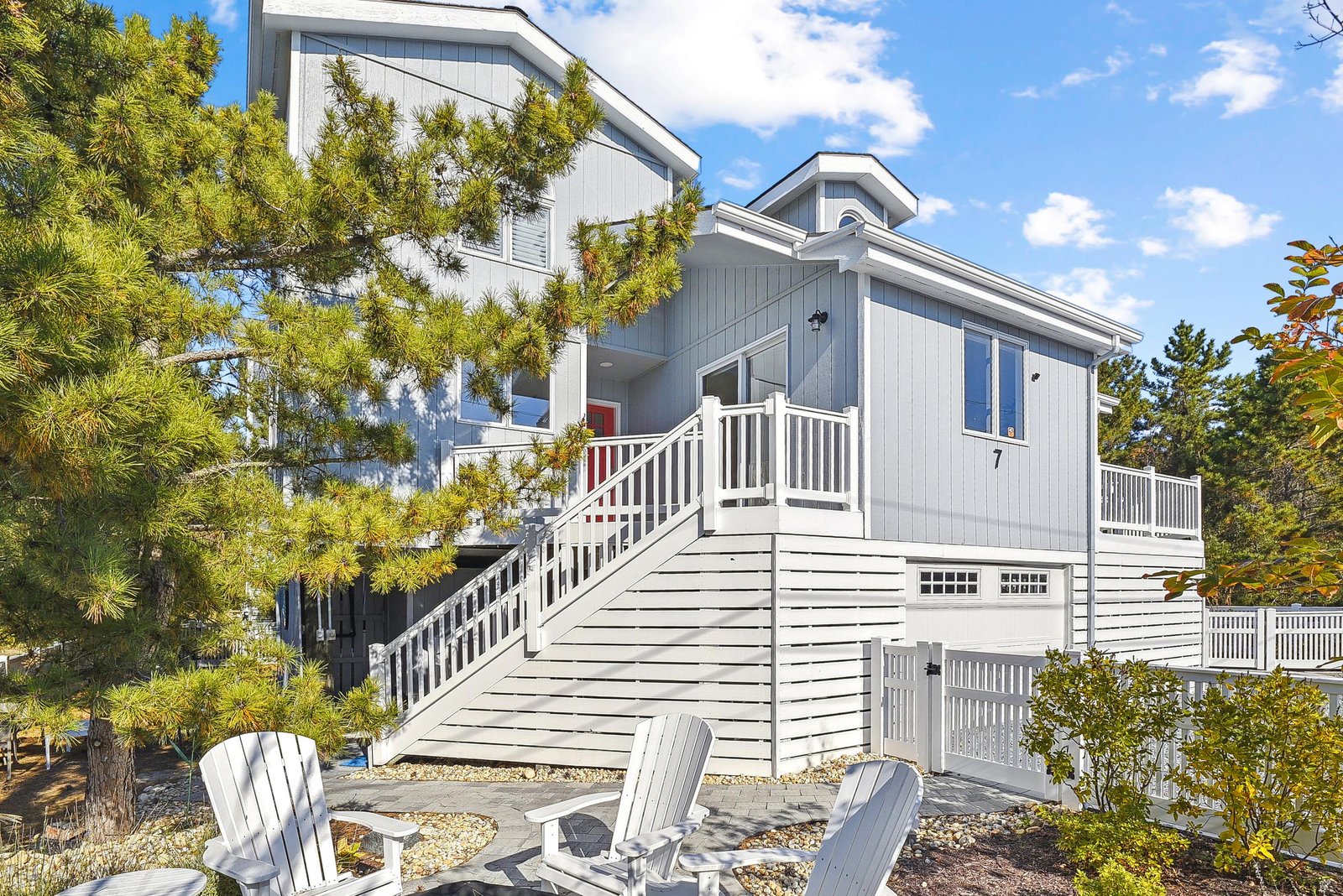 Modern beach cottage with private patio, surrounded by lush greenery under bright blue skies—your coastal retreat awaits.
