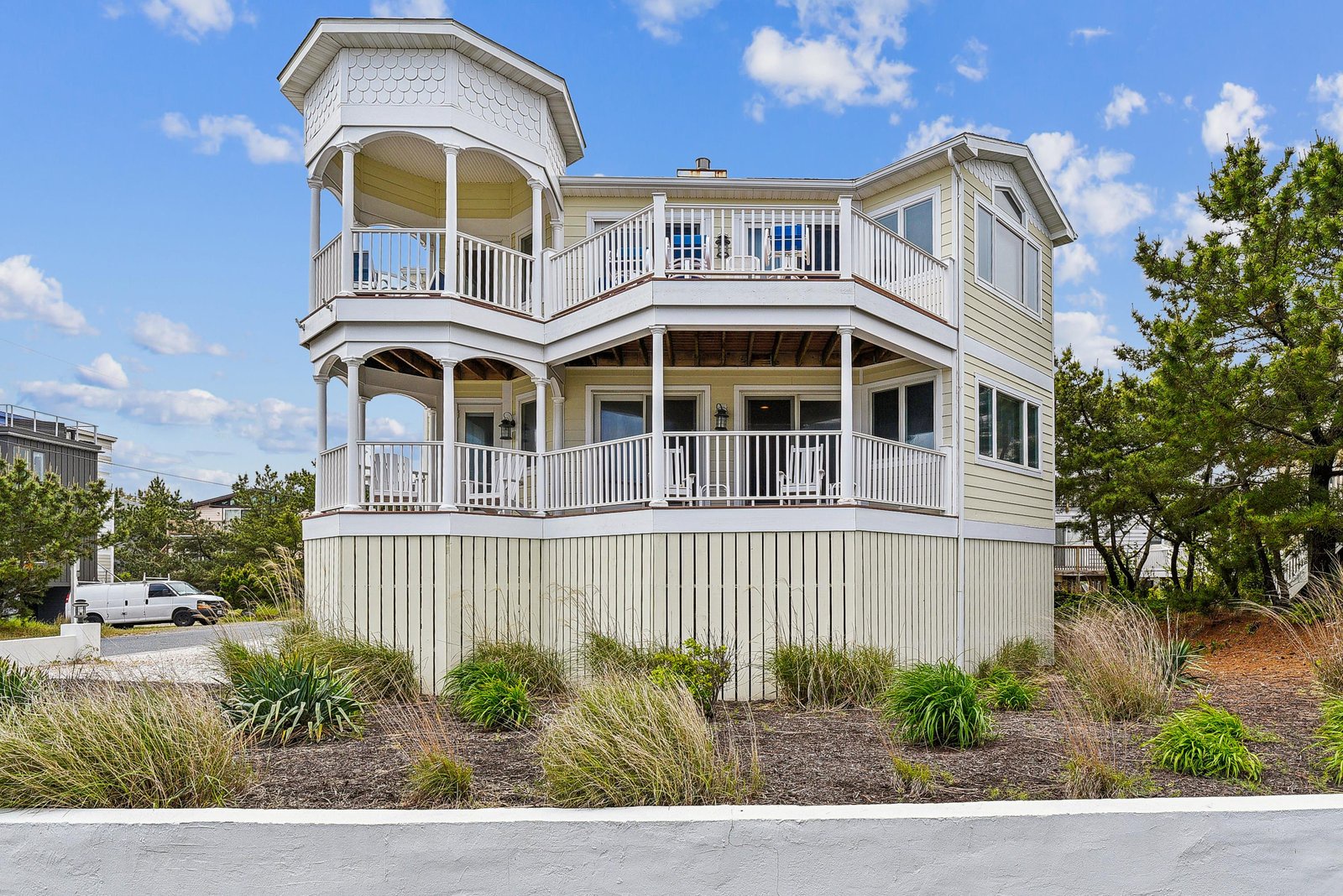 A charming beachside property featuring classic coastal architecture with multiple balconies and surrounded by natural dune vegetation, offering a welcoming arrival experience.