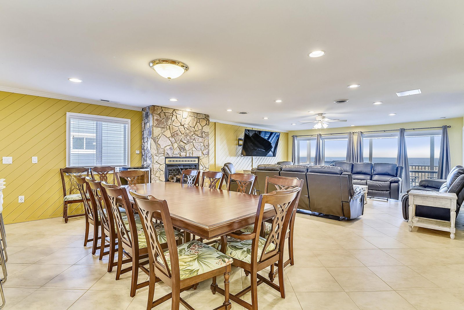 Gather around the expansive dining table for meals and games, then sink into plush recliners while enjoying ocean views through floor-to-ceiling windows. The open layout and cozy stone fireplace invite your whole group to relax together.