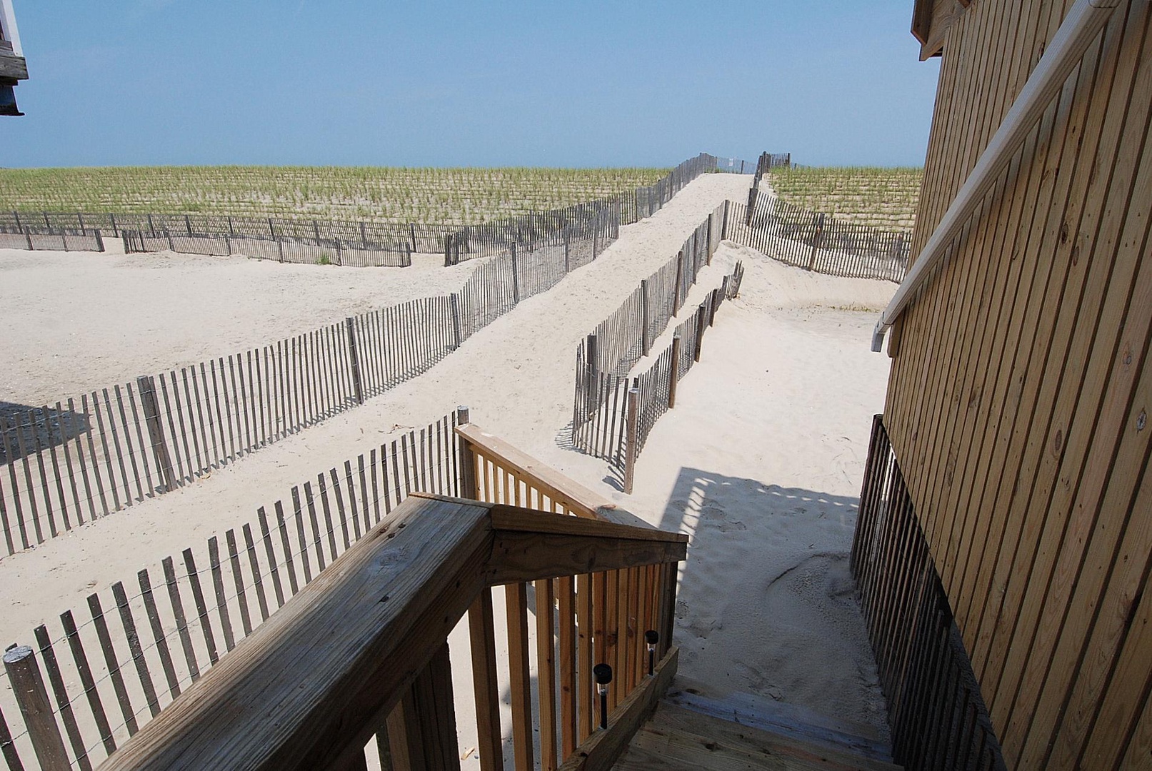 Wooden boardwalk leads through sandy dunes protected by fencing, providing direct beach access steps from the property.