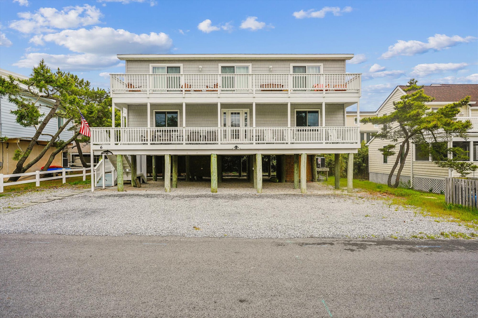 A spacious three-story coastal property with elevated construction, wraparound balconies, and ample parking for multiple vehicles beneath the raised foundation.