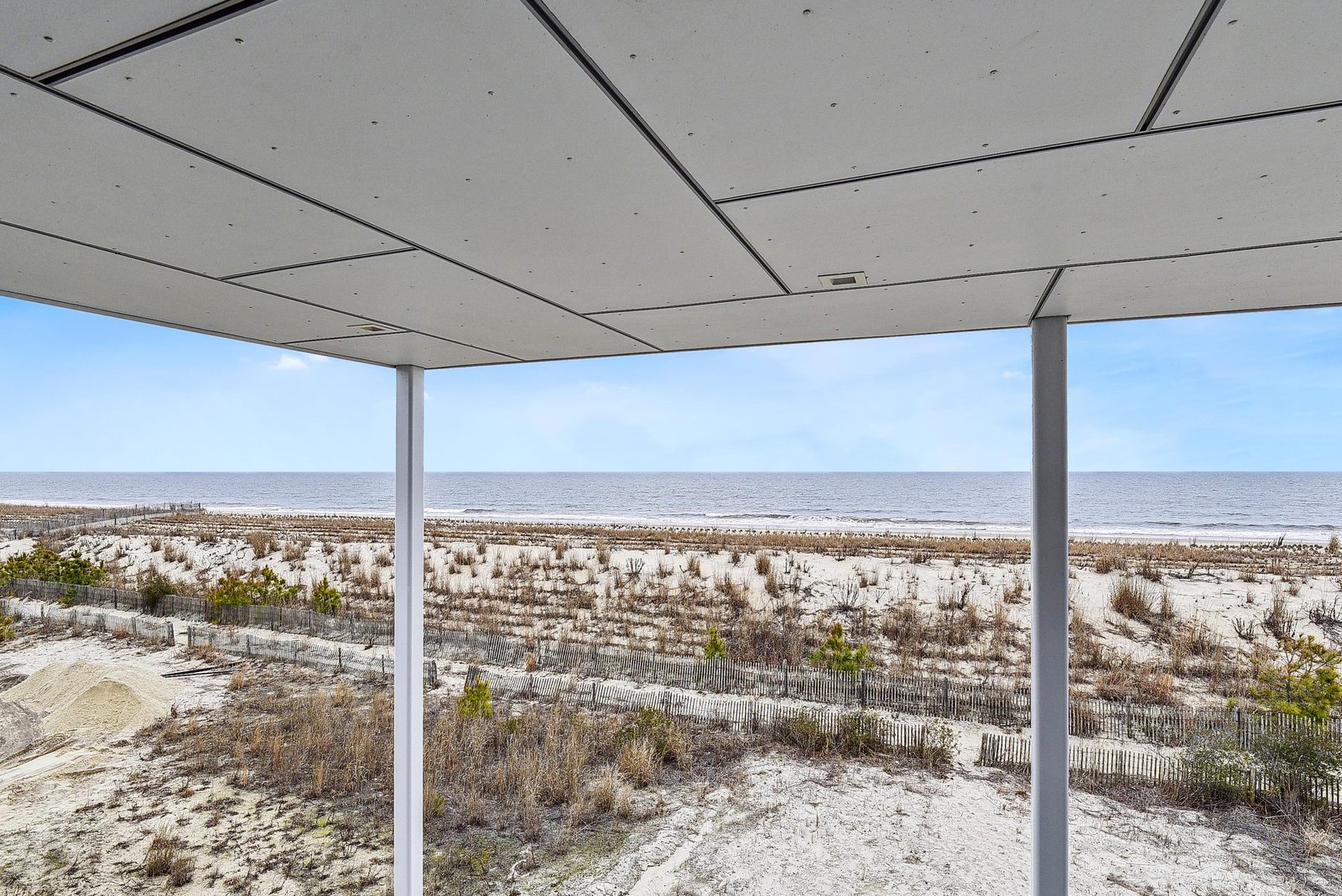 The property offers a covered terrace with expansive ocean and beach views across sandy dunes and coastal vegetation.