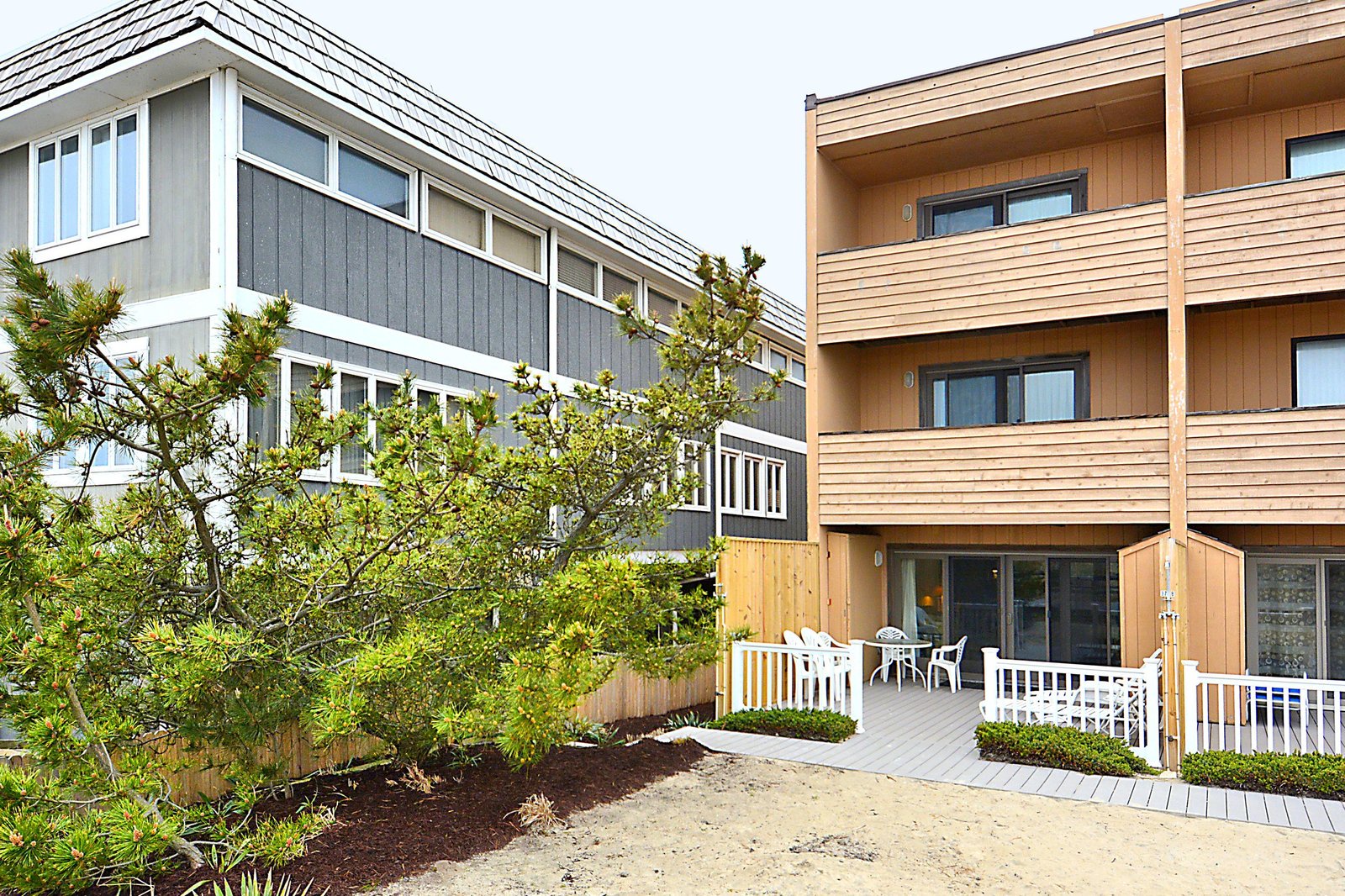 Two modern multi-level buildings with distinct architectural styles frame a beautifully landscaped courtyard area, each offering private balconies and ground-floor patios.