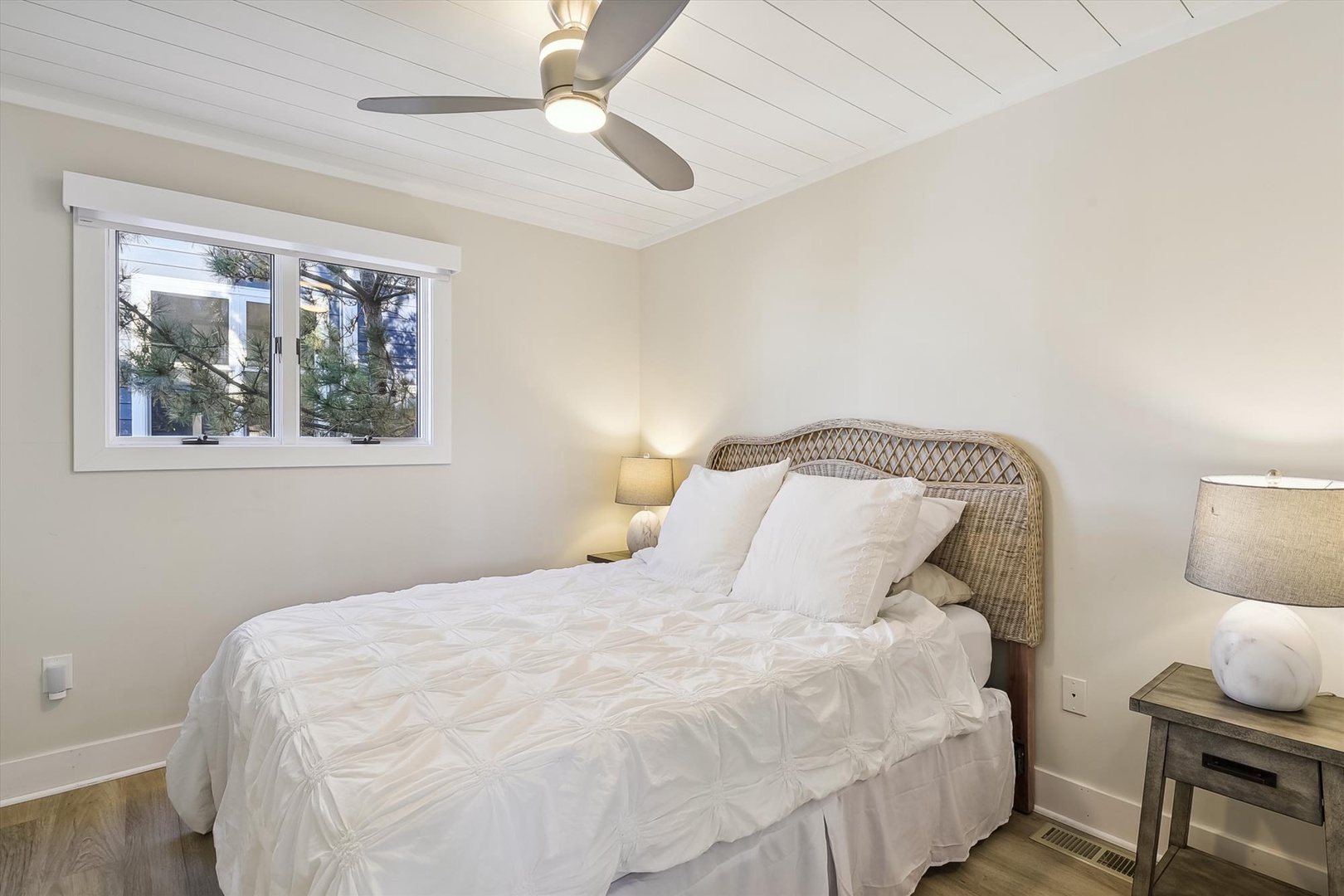 Sink into crisp white linens in your serene bedroom, where a gentle ceiling fan and natural light create your perfect retreat after a day of coastal adventures.