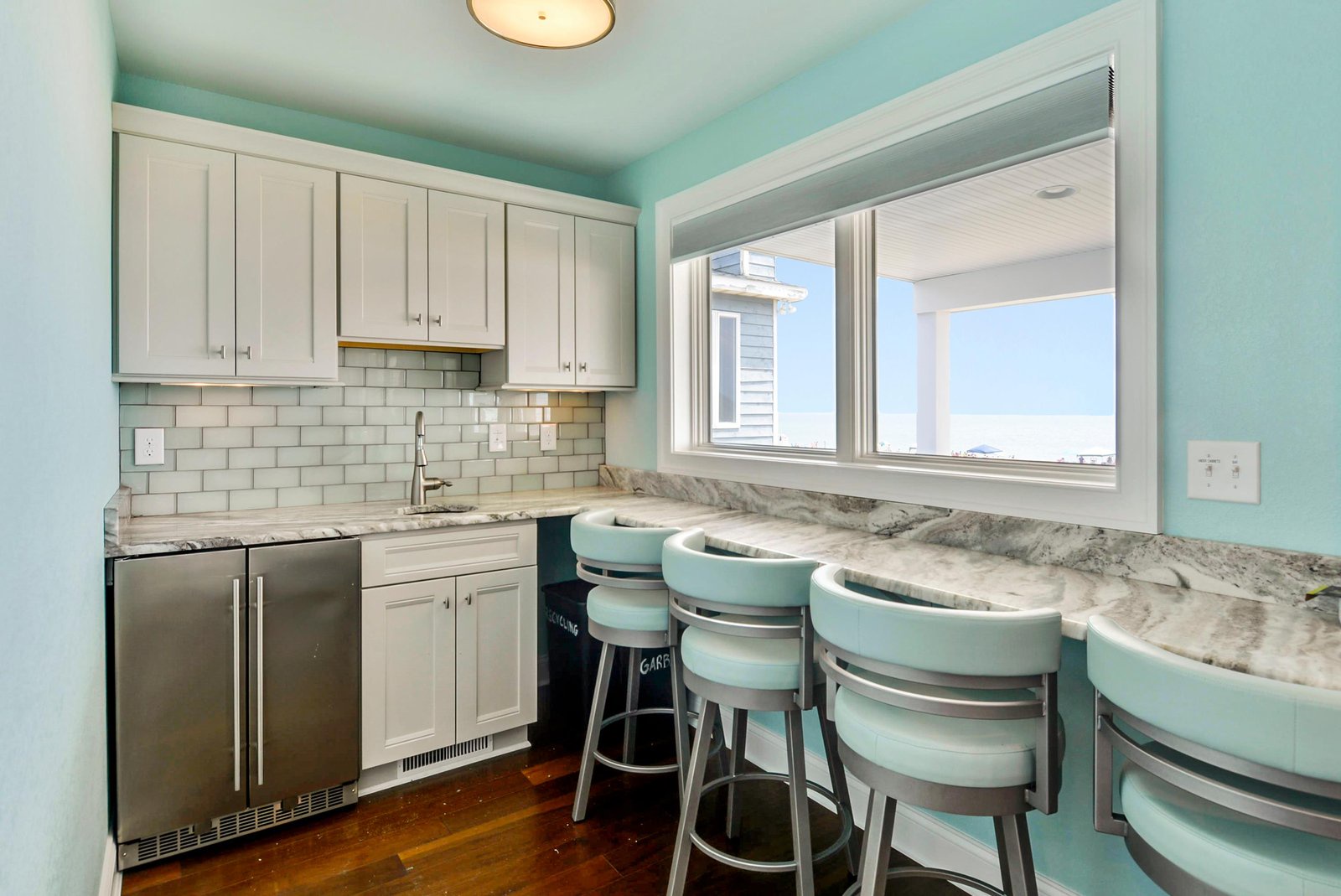 Sip your morning coffee at the cozy breakfast bar in this cheerful kitchenette, where soft turquoise walls and classic white cabinetry create a bright, inviting space for quick bites and casual meals.