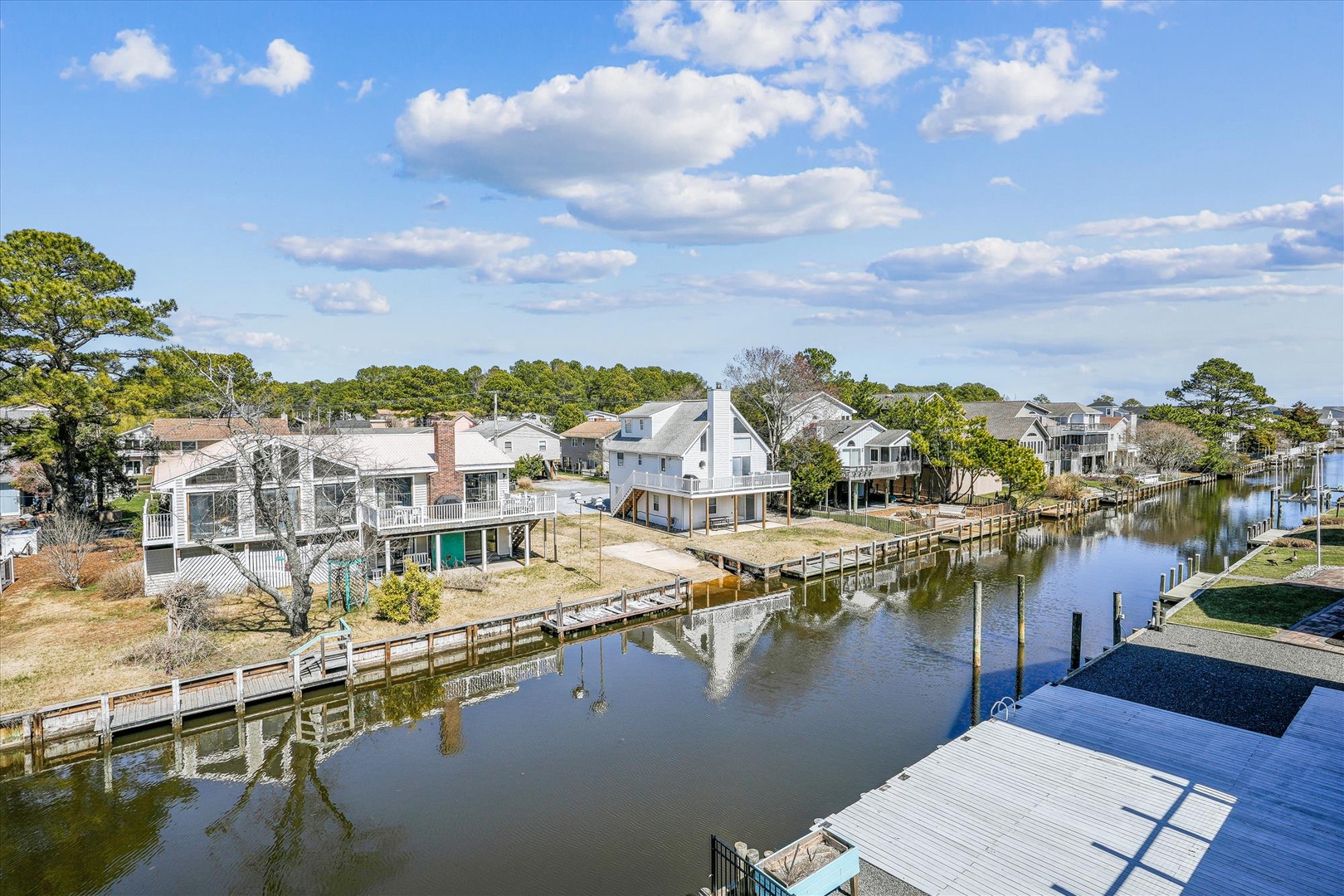Aerial view of a peaceful waterfront community with private docks, lush greenery, and charming homes nestled along a tranquil canal under a beautiful blue sky.