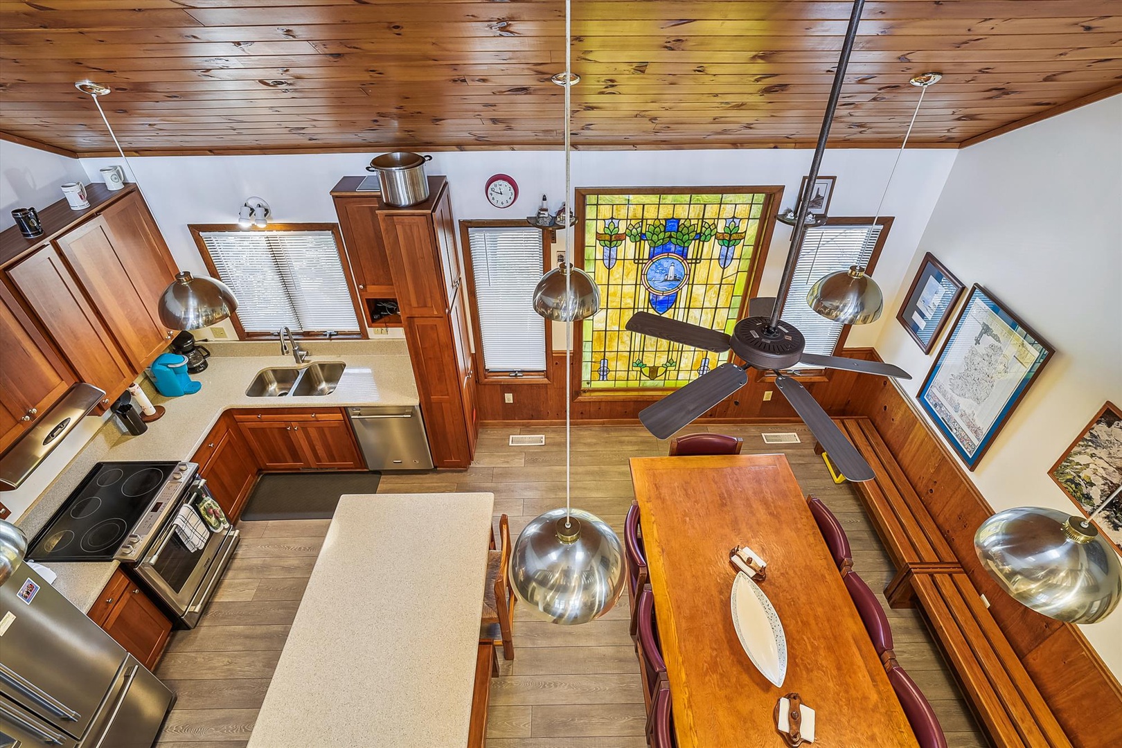 An aerial view showcases a warm, open-concept space where knotty pine ceilings and rich wood cabinetry meet modern stainless appliances. A stunning stained-glass accent adds character above the polished dining table, ready for your next meal.