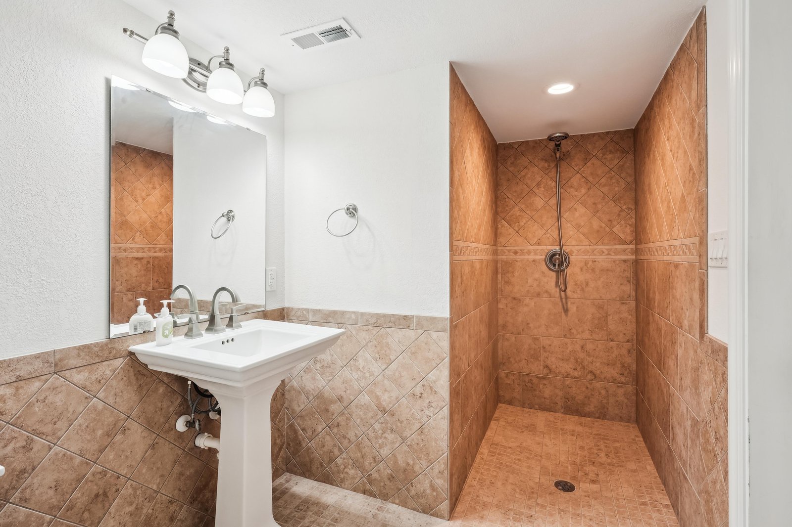 Step into your private sanctuary with warm terracotta tiling, a spacious walk-in shower, and elegant pedestal sink—perfect for refreshing after sunny days exploring the coast.
