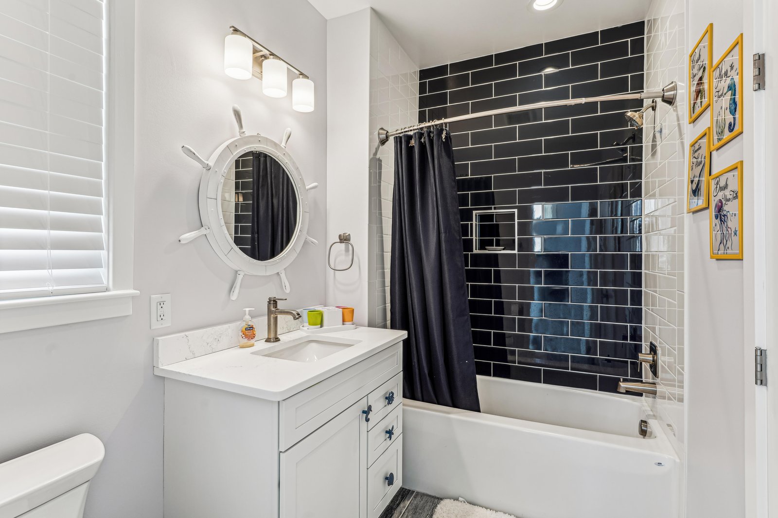 Step into a bright, nautical-inspired bathroom with subway tile, a deep soaking tub, and charming ship's wheel mirror. Your coastal retreat starts here.