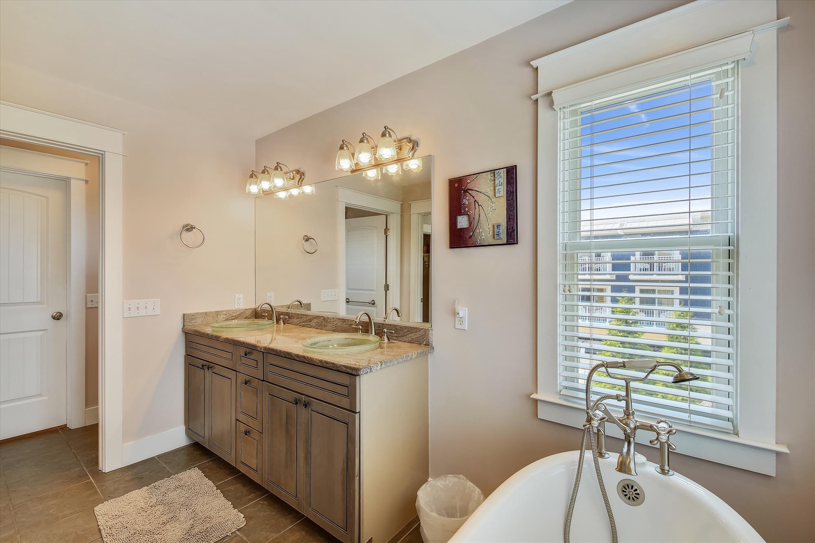 Soak in style—your elegant bathroom features a soaking tub by a sunny window, dual vanities with modern fixtures, and warm lighting for a spa-like retreat.