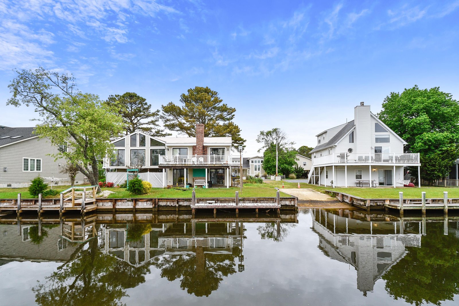 Waterfront retreat with private docks on a peaceful canal, framed by mature trees and spacious lawns under clear skies.