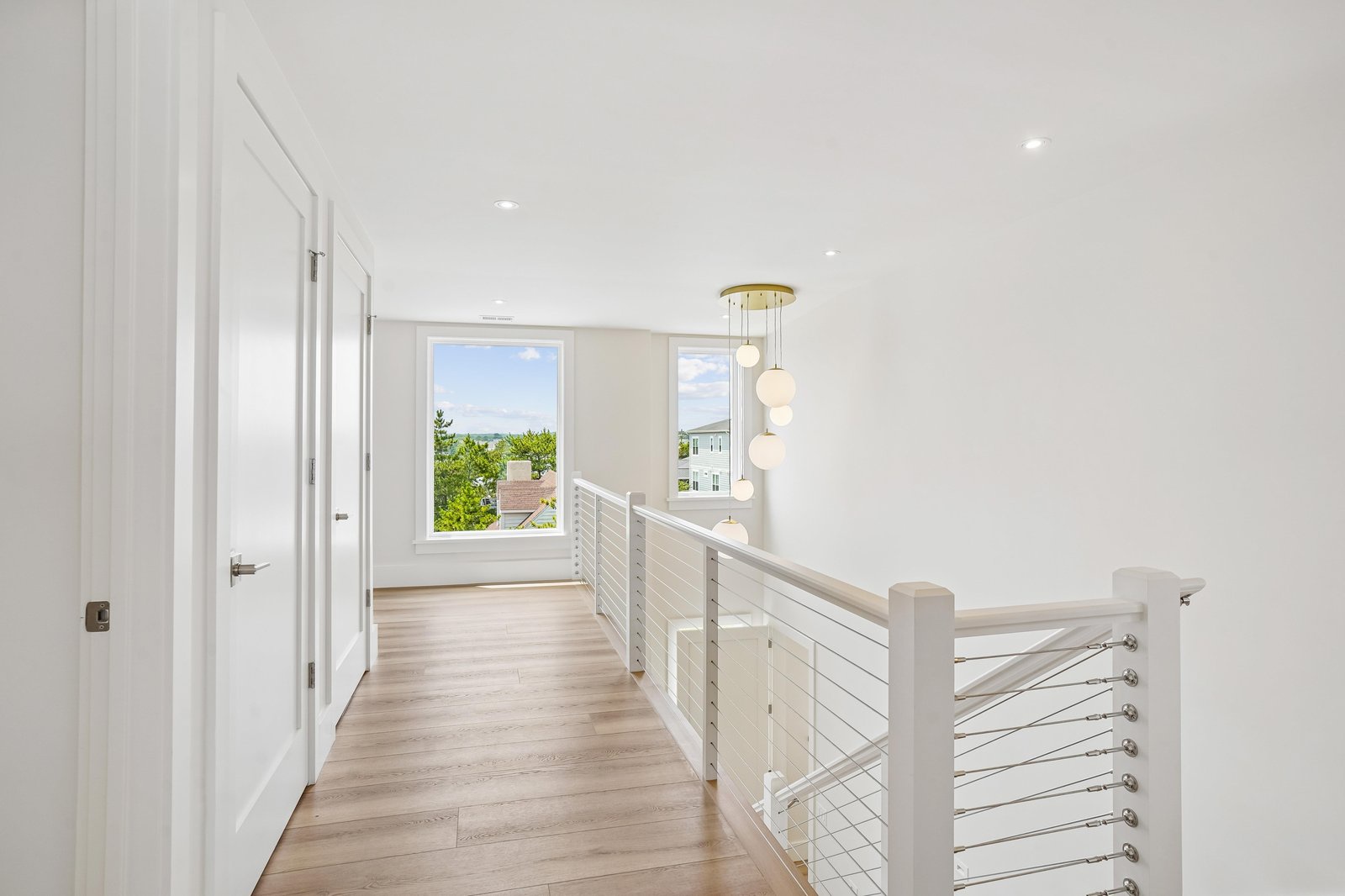 A bright hallway leads your eye to serene neighborhood views through the window, where soft light and modern fixtures create a calm, welcoming transition between rooms.