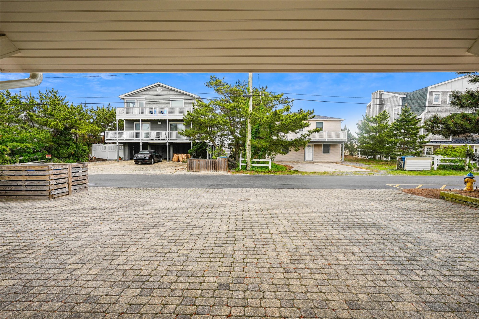 The property is located in a quiet residential coastal neighborhood with paver parking and nearby beach homes surrounded by lush greenery.
