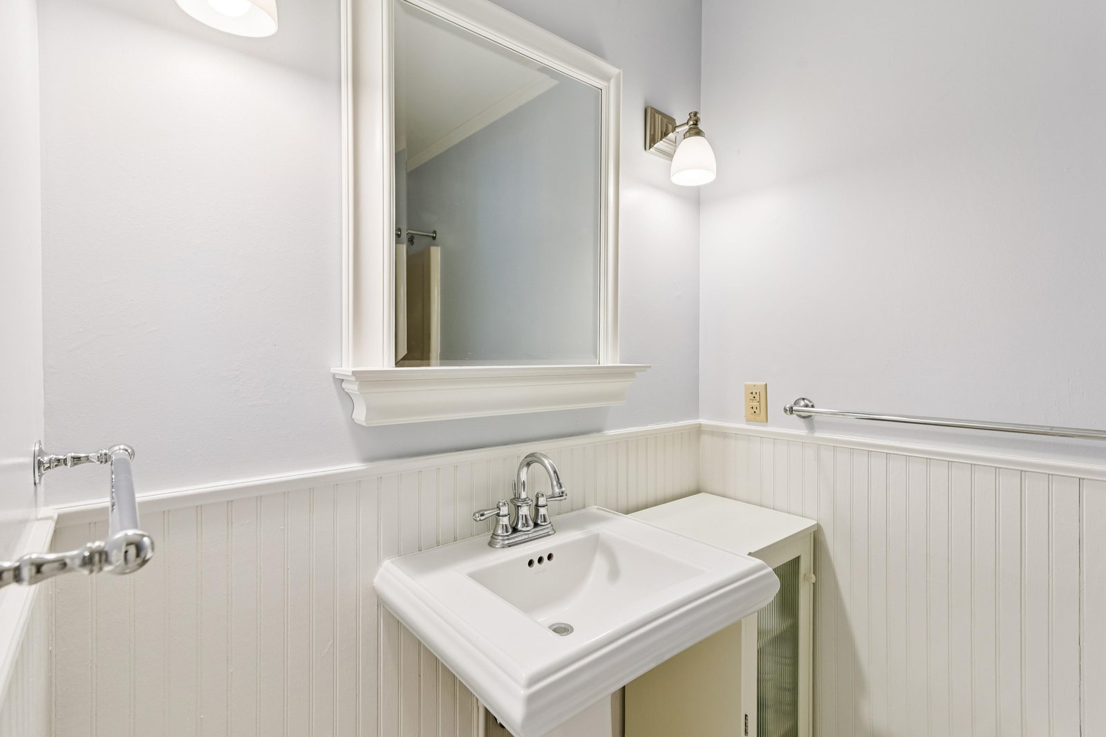 Freshen up in your private bathroom with classic beadboard wainscoting, a crisp pedestal sink, and soft lighting—everything you need for a comfortable stay.