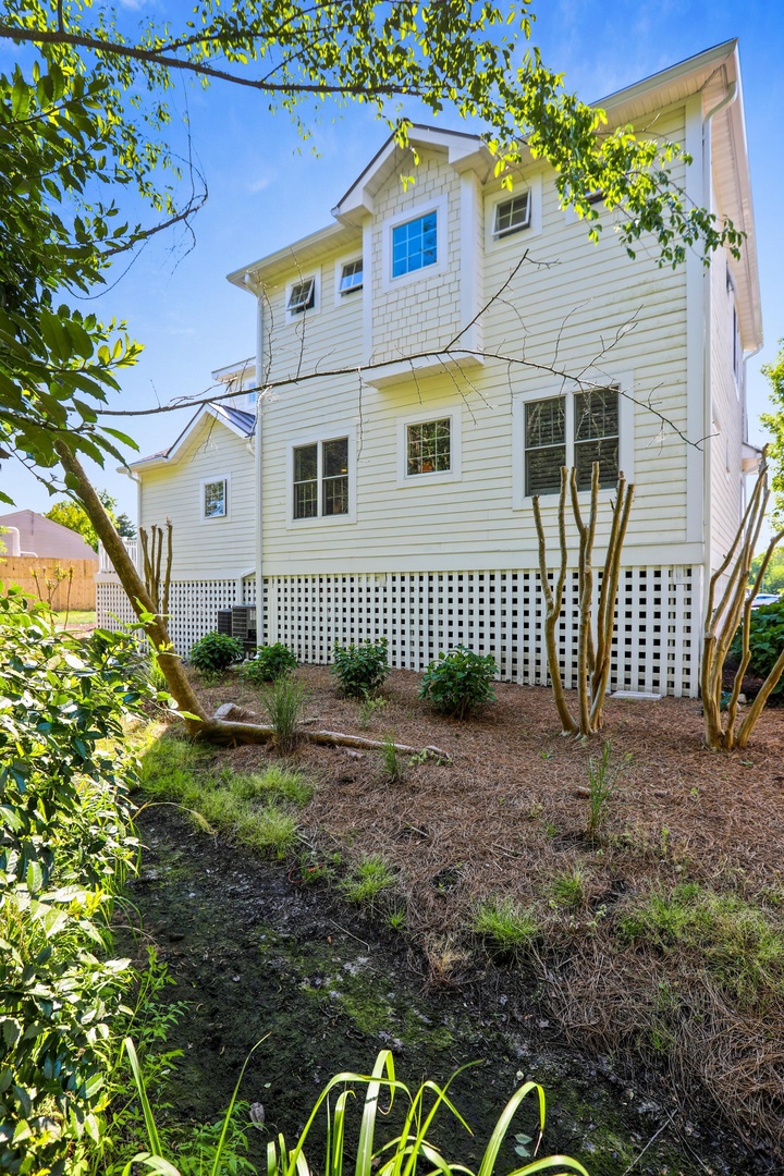 A two-story coastal property with crisp white siding, framed by lush greenery and mature trees in a peaceful residential setting.
