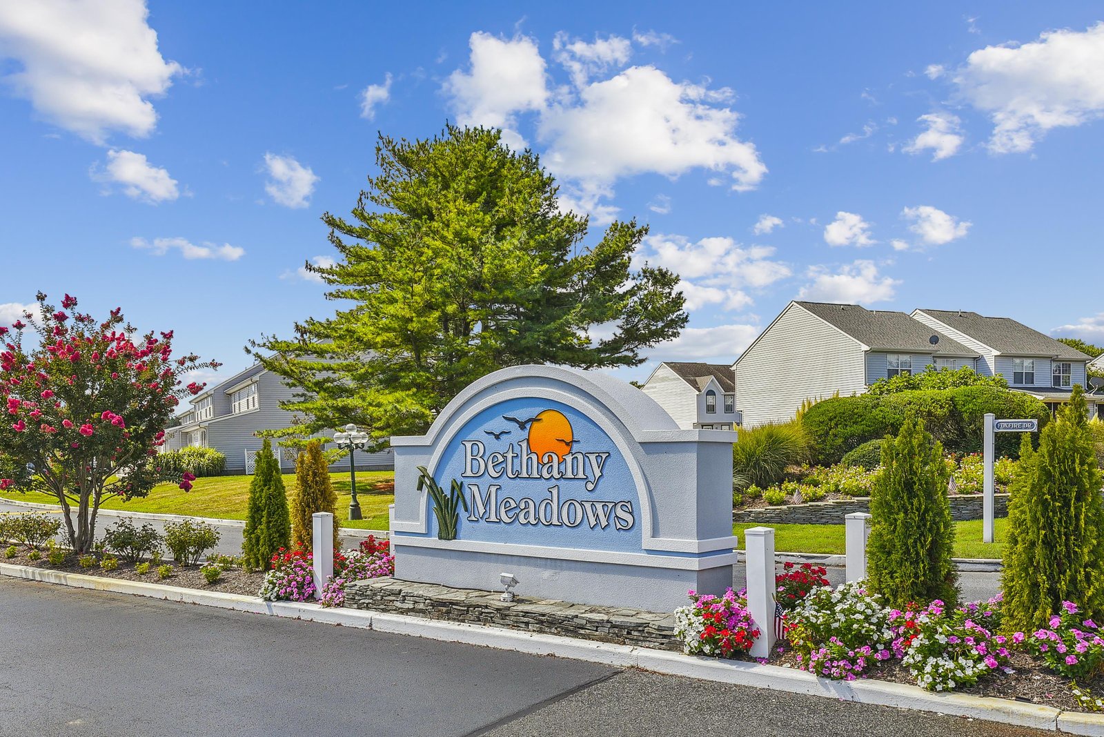 The Bethany Meadows community entrance sign welcomes arrivals with colorful blooms and manicured landscaping under a bright blue sky.