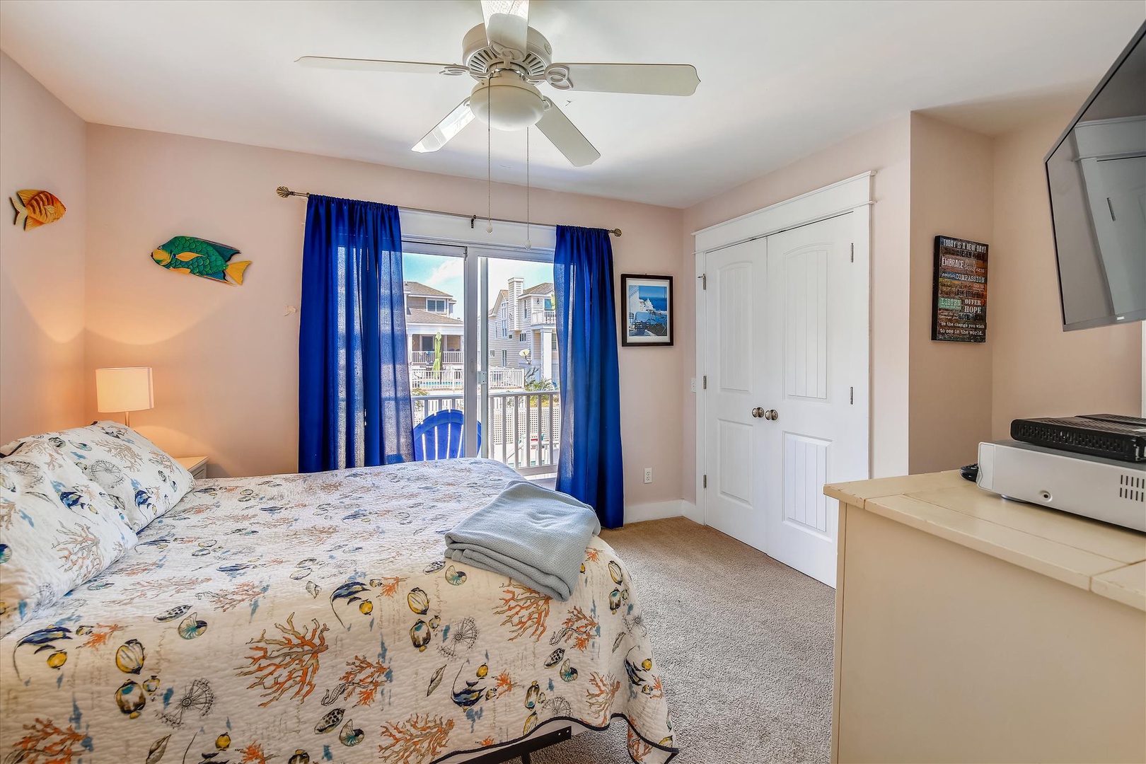 Step into your bright, coastal-themed bedroom with a plush bed, ceiling fan, and balcony access—your perfect retreat after a day of adventure.