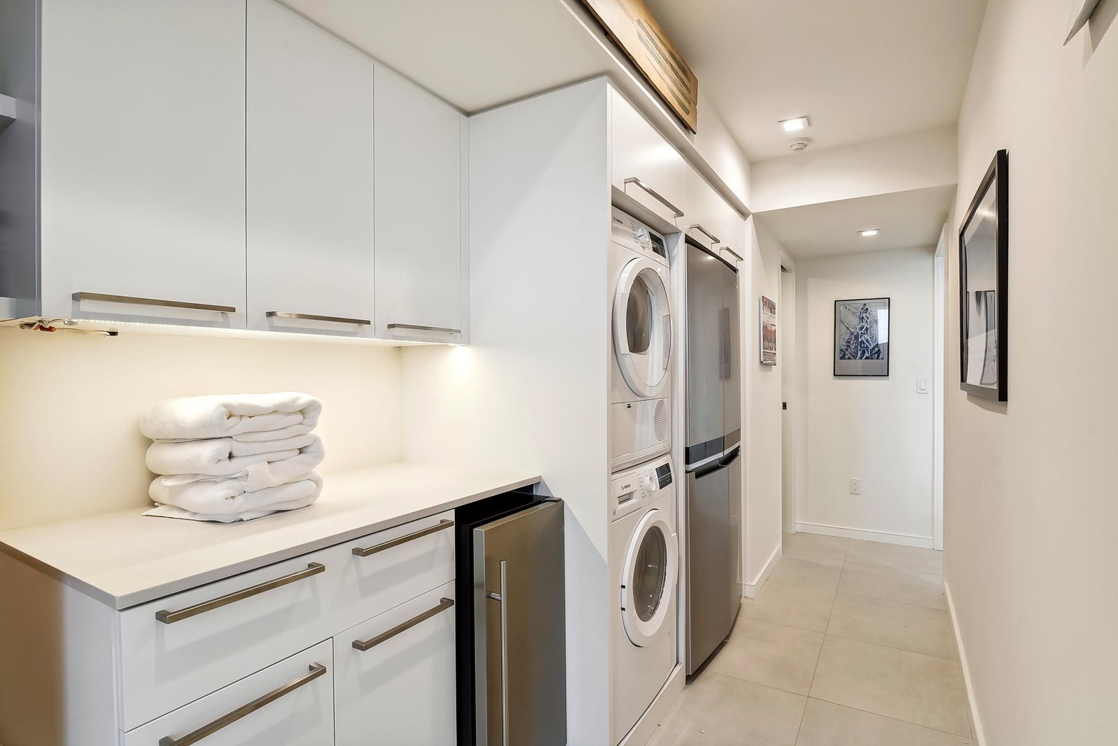 Your laundry stays effortless in this sleek, well-lit space with stacked washer and dryer, ample storage, and neatly folded towels always at the ready.