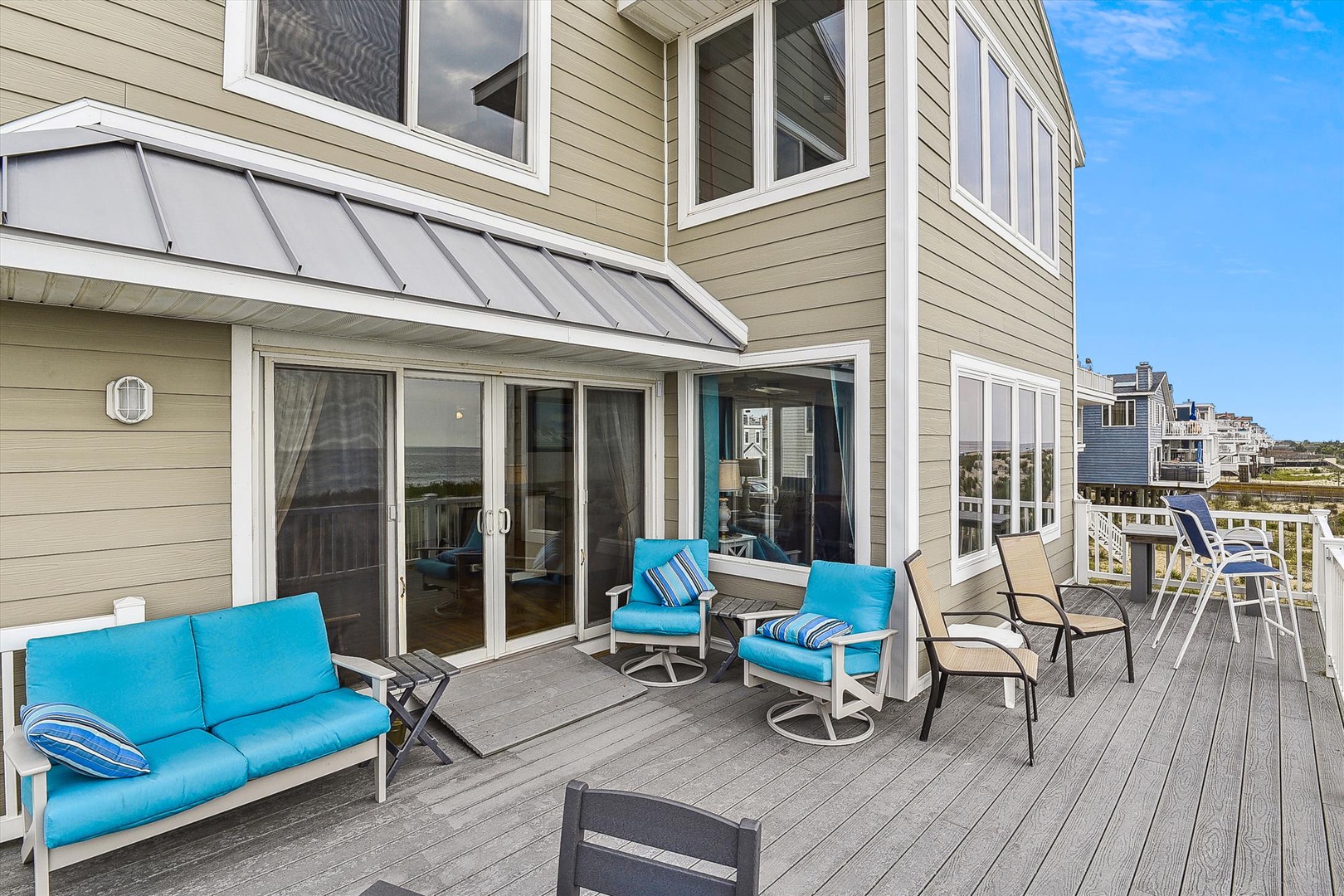 Spacious deck with vibrant turquoise seating invites you to relax outdoors, complete with dining area and coastal views beyond—your perfect spot for morning coffee or sunset gatherings.