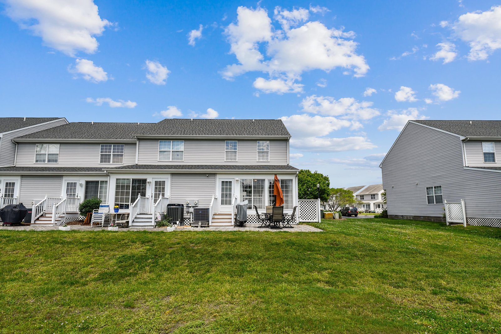 A two-story residential building featuring multiple rental units with private patios and green lawn spaces in a quiet suburban neighborhood.