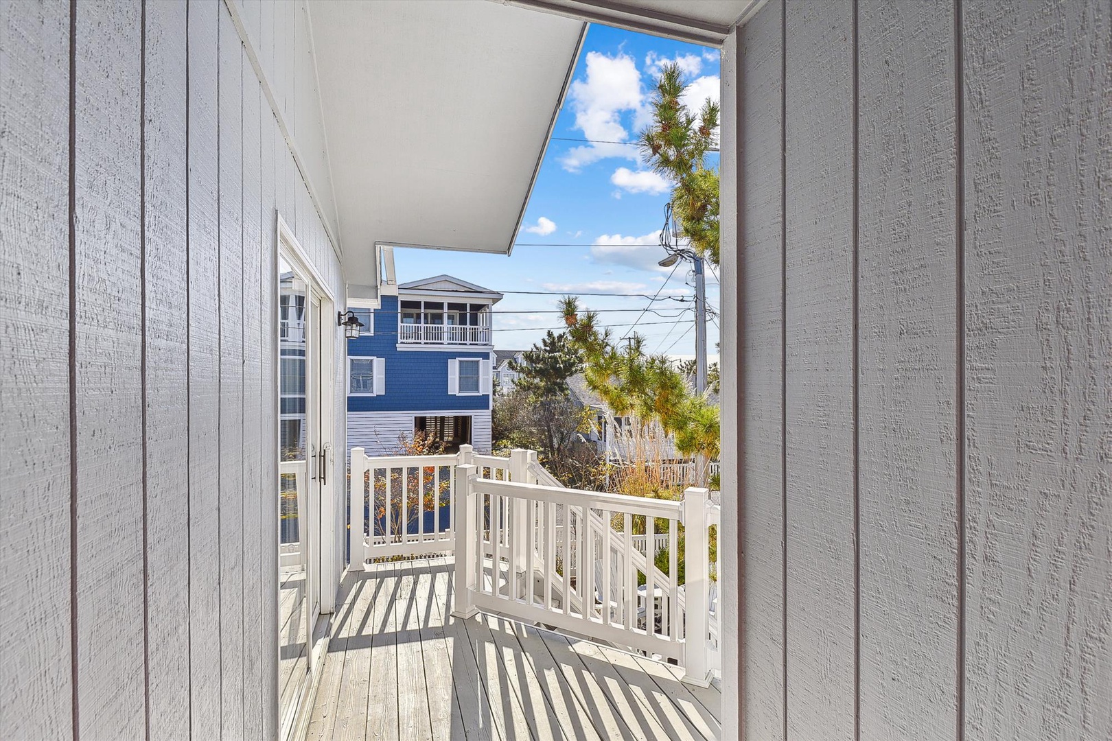 Step onto your private balcony, where sunlight filters through pine branches and a peaceful coastal neighborhood unfolds beyond the white railings—perfect for morning coffee or evening relaxation.