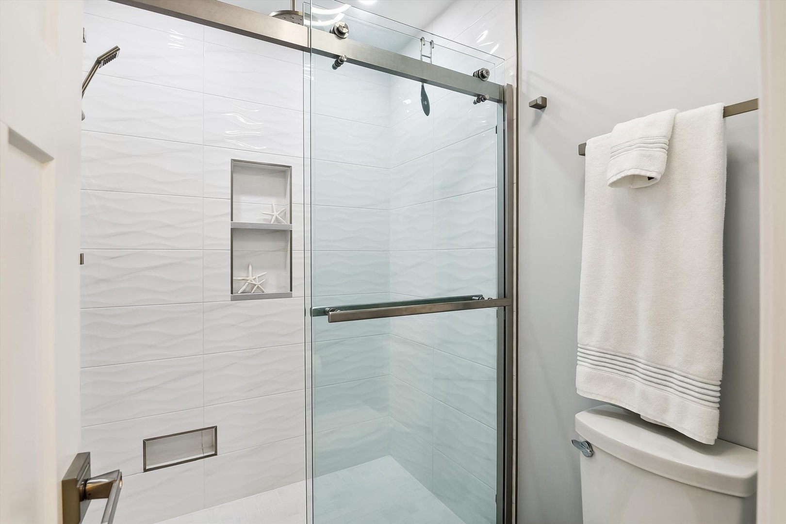Step into your elegant glass-enclosed shower with coastal charm—starfish details and plush towels await your refreshing retreat.