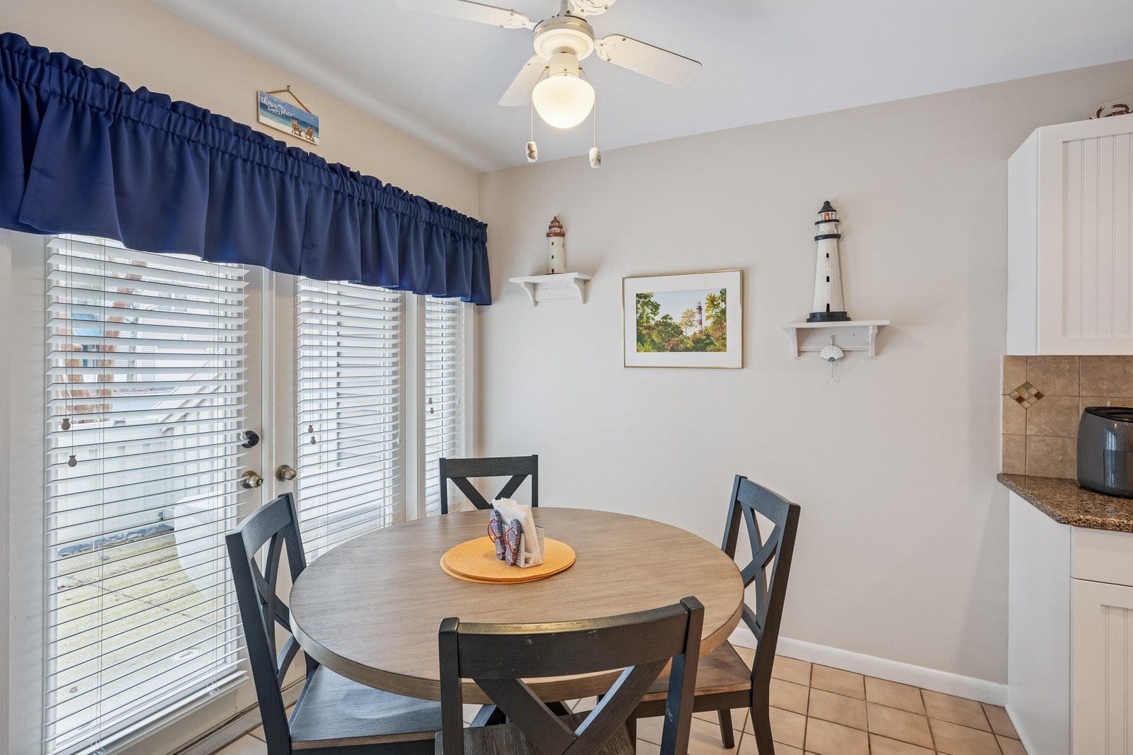 Gather around this cozy dining table for morning coffee or a leisurely meal. Natural light spills in through the doors, while coastal touches create a welcoming, homey atmosphere for your stay.