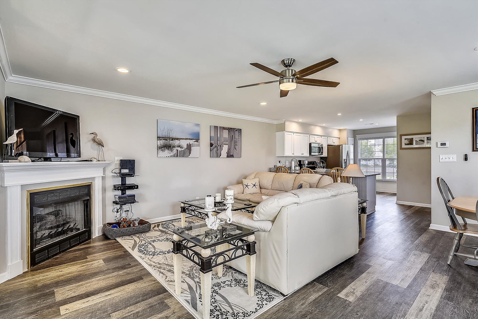 Sink into plush sofas by the fireplace, where natural light and coastal artwork set a serene tone. Your open-concept retreat flows seamlessly into the kitchen and dining area.