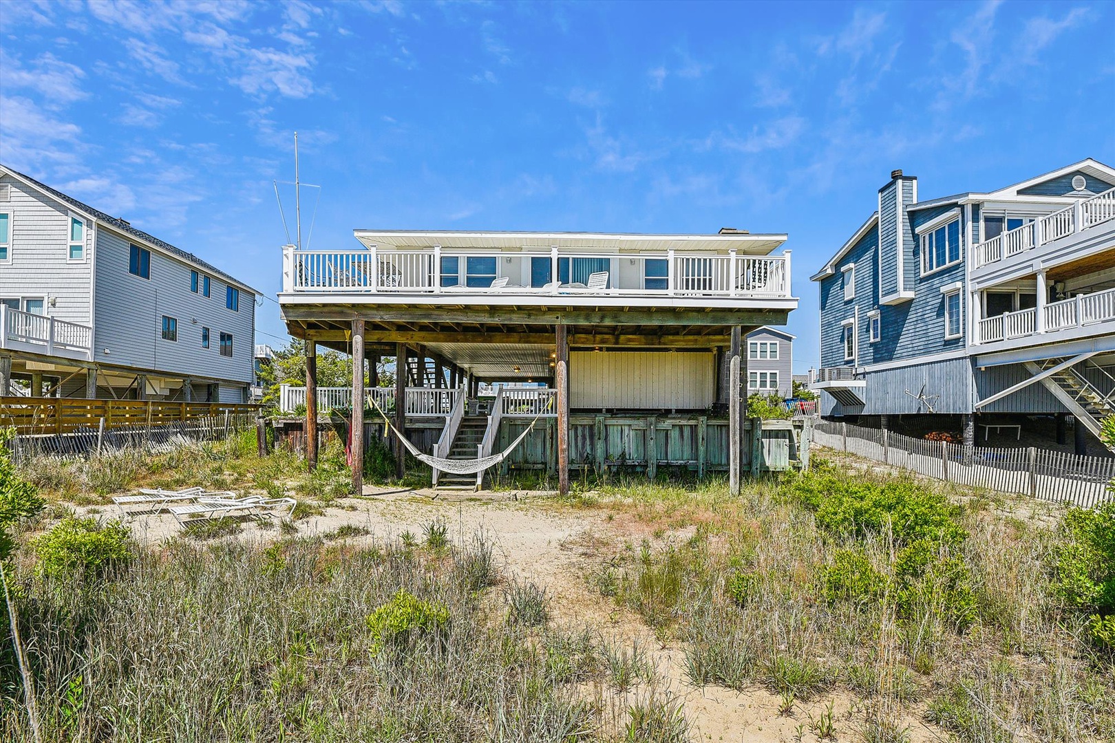 Beachfront property with direct sandy access and elevated deck overlooking the shore, nestled in a friendly coastal neighborhood with neighboring beach houses nearby.