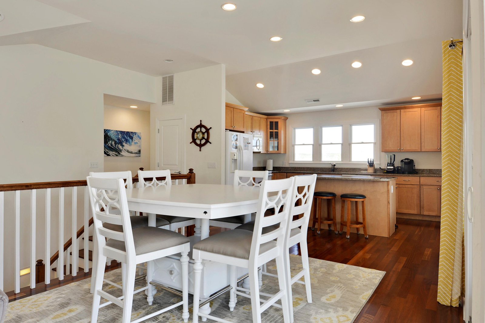 Spacious dining and kitchen area with warm wood tones, coastal charm, granite counters, and modern appliances—perfect for morning coffee and delicious home-cooked meals.