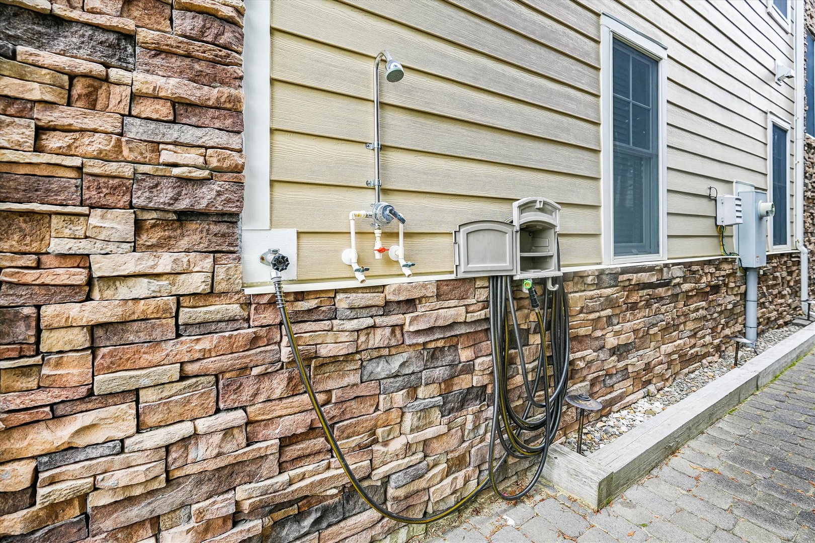 The property features attractive stone-accent siding and a convenient outdoor hose connection along the exterior walkway, blending functional utility with stylish curb appeal.