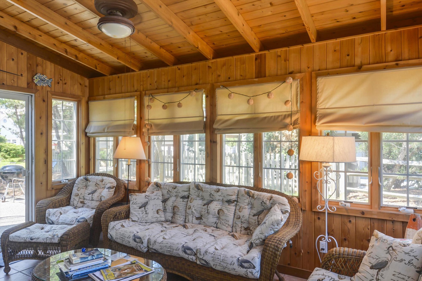 Relax in this cozy sunlit space with charming wicker seating and warm wood details. Large windows frame peaceful outdoor views, inviting you to unwind in comfort and natural light.