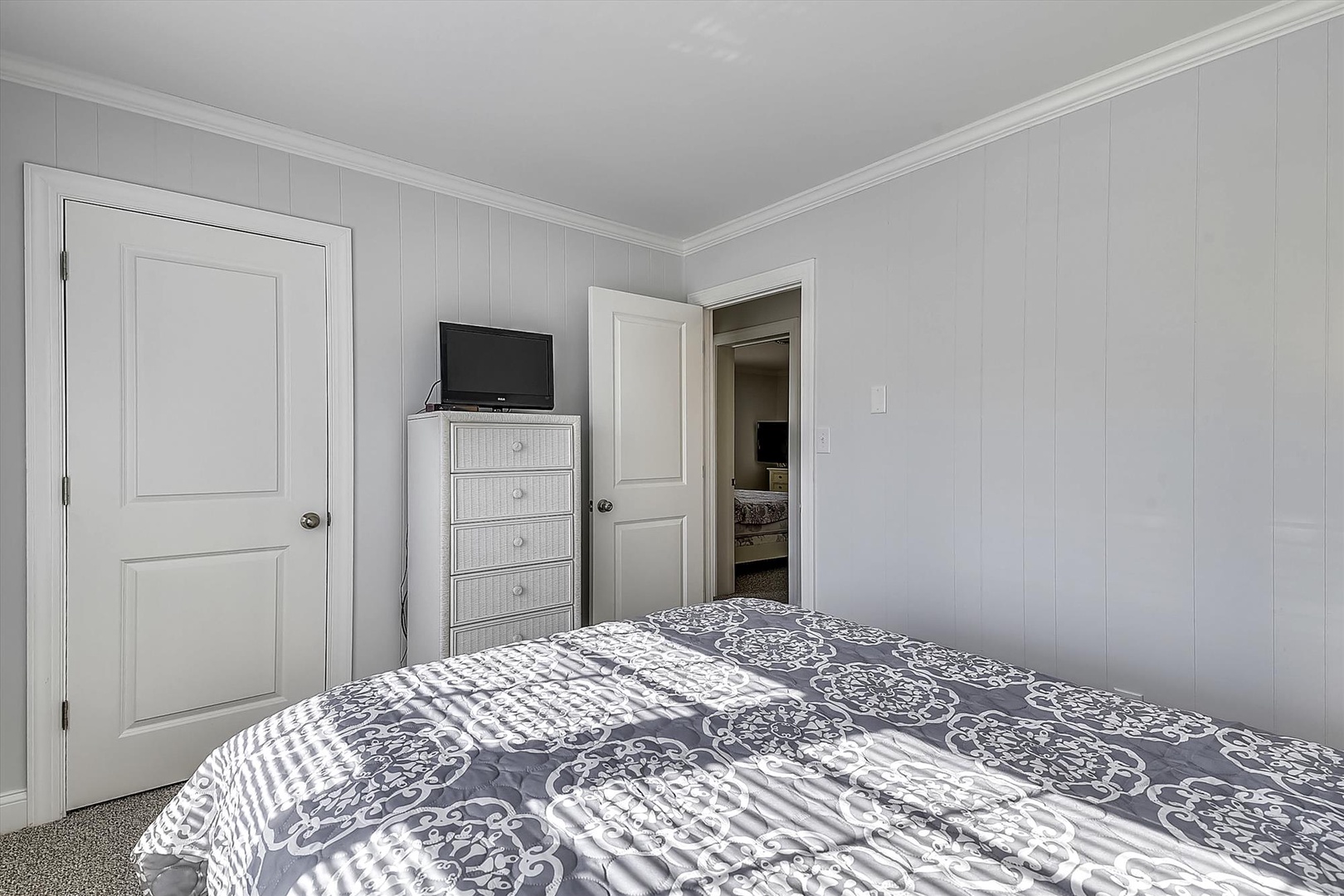 Your peaceful bedroom features a comfortable bed with elegant bedding, TV for entertainment, and thoughtful storage with a charming white dresser.