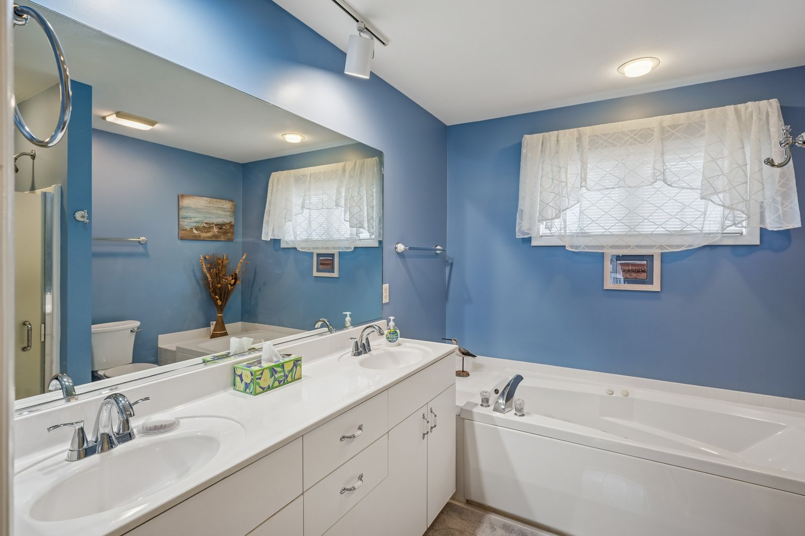 Unwind in your spa-like bathroom featuring a soaking tub, dual vanities, and calming blue walls that create your perfect retreat.