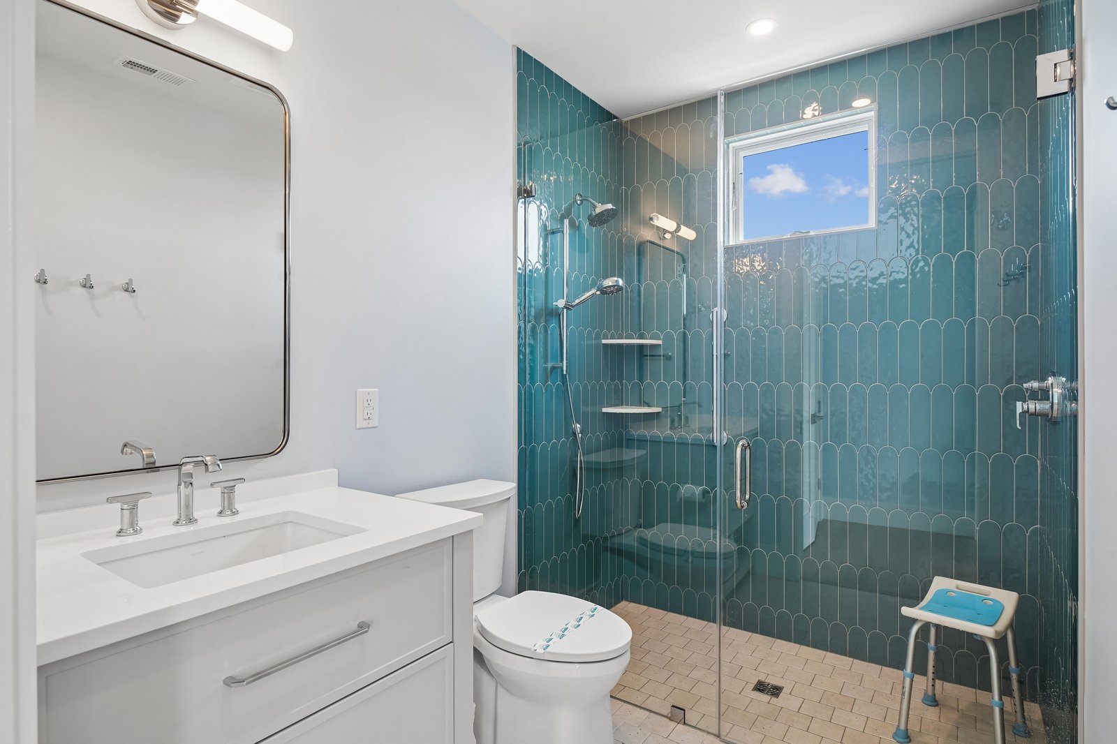 Your private bathroom features calming ocean-inspired teal tiles and a spacious walk-in shower with dual fixtures, blending spa-like elegance with everyday comfort.