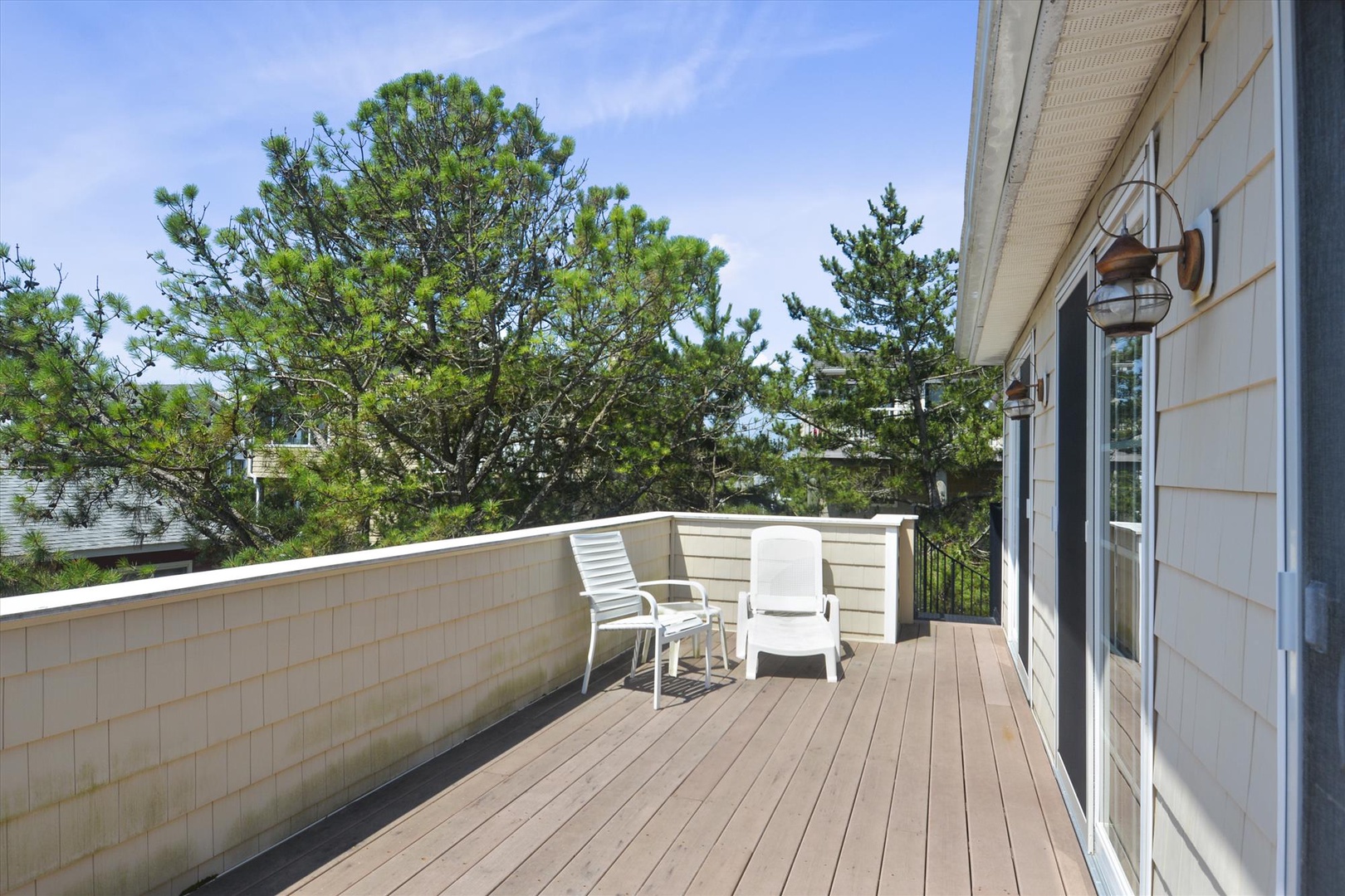 Step out onto your private deck where coastal pines frame the horizon and white lounge chairs invite unhurried mornings with coffee in hand.