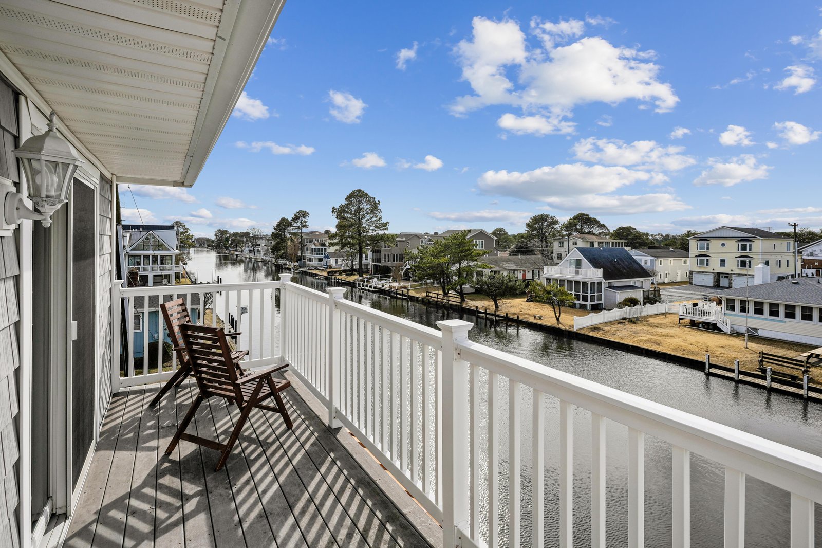 A serene waterfront neighborhood with docks, trees, and charming coastal homes under expansive blue skies punctuated by soft clouds.