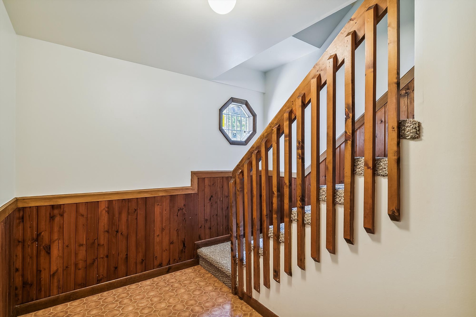 Natural light pours through the octagonal window as you ascend the warm wooden staircase, where rustic charm meets comfort in this inviting multi-level retreat.