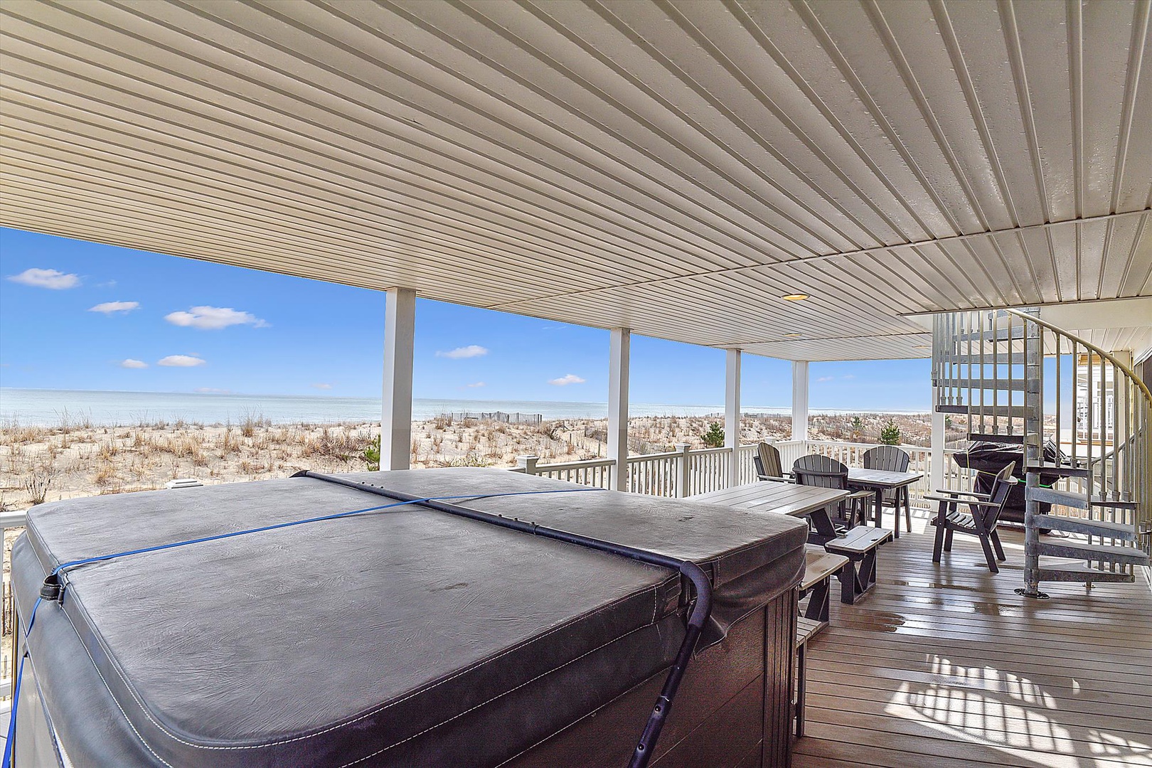 Private beachfront deck features a covered hot tub and dining area with direct access to sandy shores, where you can unwind to panoramic coastal views.