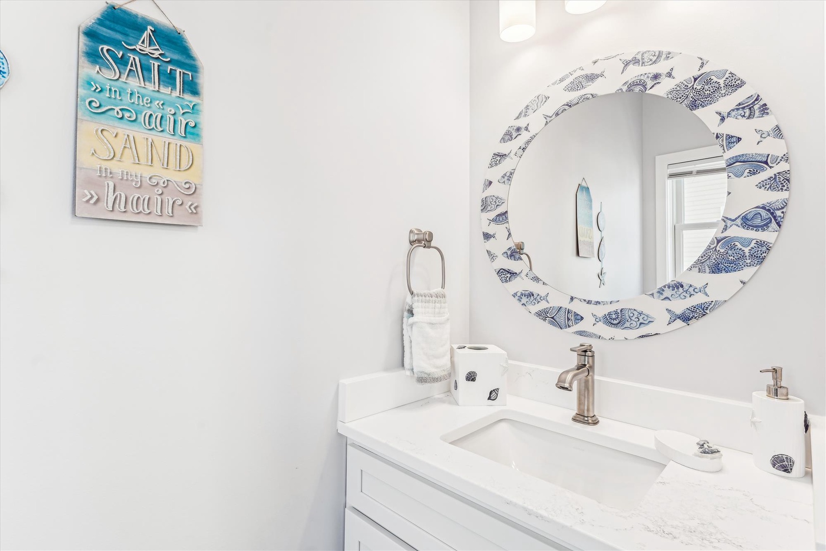 Freshen up in this bright coastal-inspired bathroom featuring a charming fish-motif mirror and beachy décor that'll make you feel right at home by the shore.