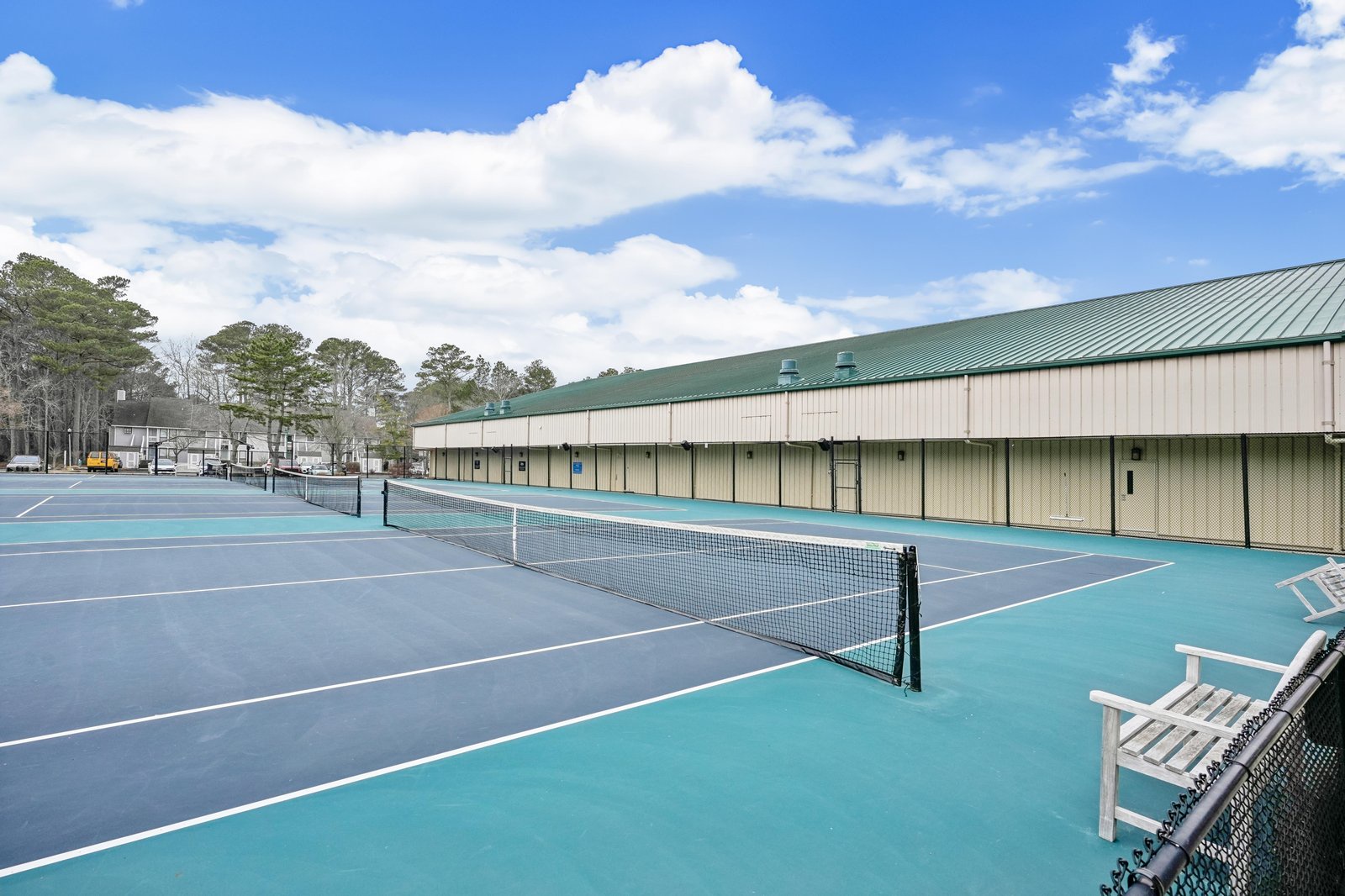 Well-maintained tennis courts with adjacent building and scenic tree-lined surroundings, perfect for active recreation during your stay.