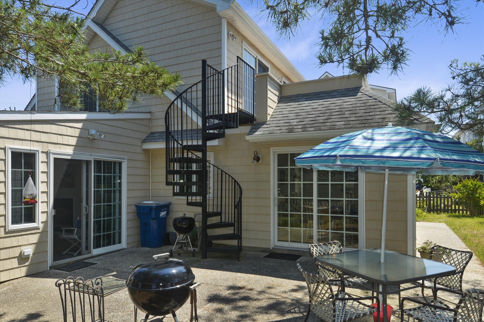 Spacious patio features outdoor dining and BBQ area, with spiral stairs leading to an upper deck overlooking lush greenery.