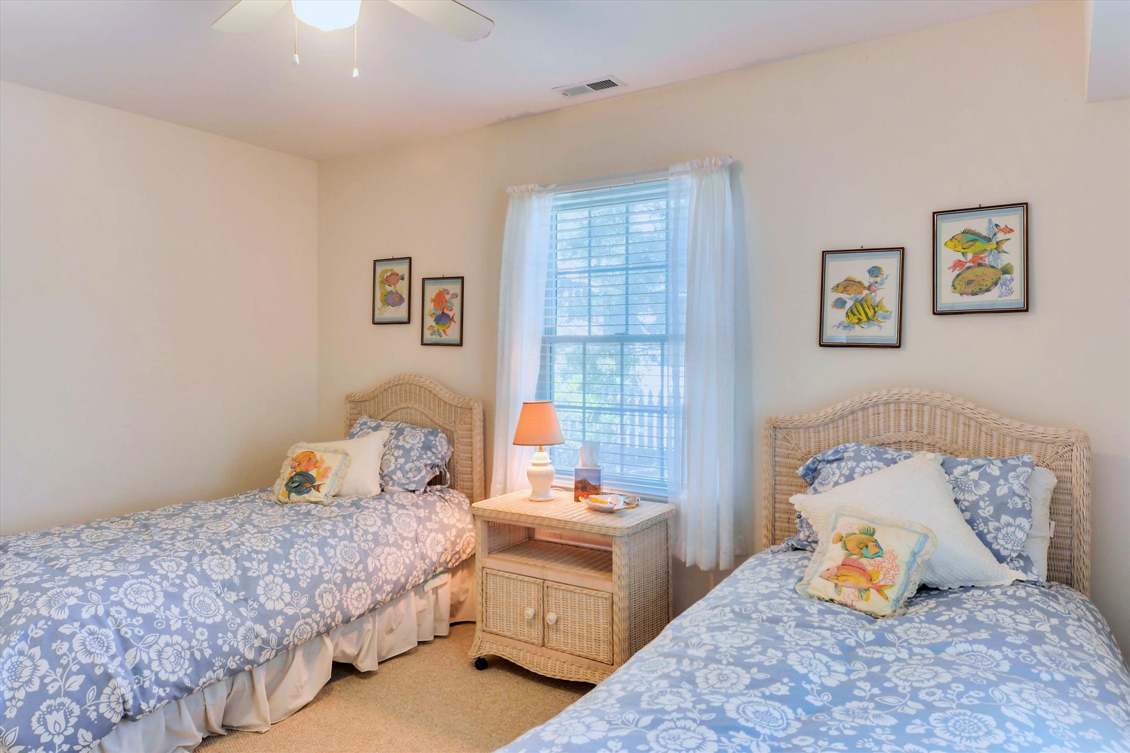 Your coastal-themed twin bedroom awaits with soft blue linens, natural wicker furnishings, and cheerful tropical fish artwork creating a breezy beach house feel perfect for relaxing after a sun-filled day.