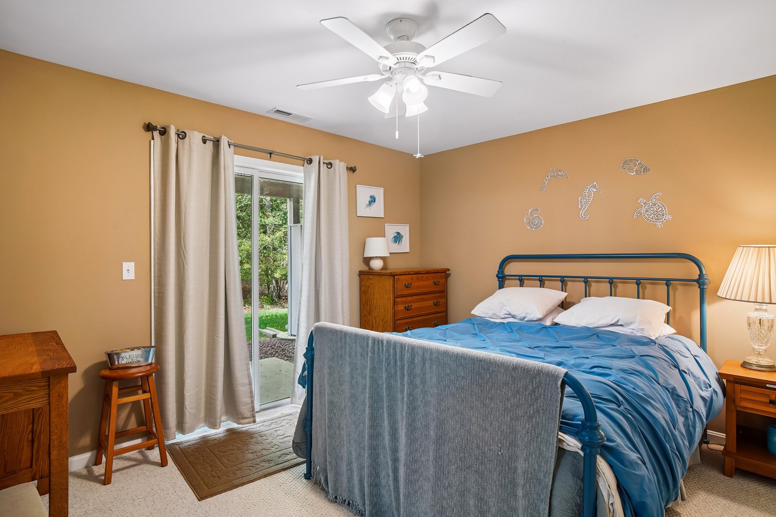 Drift off in your cozy coastal bedroom, where ocean-themed accents and soft linens create the perfect retreat. A ceiling fan keeps you comfortable while garden views add natural serenity.