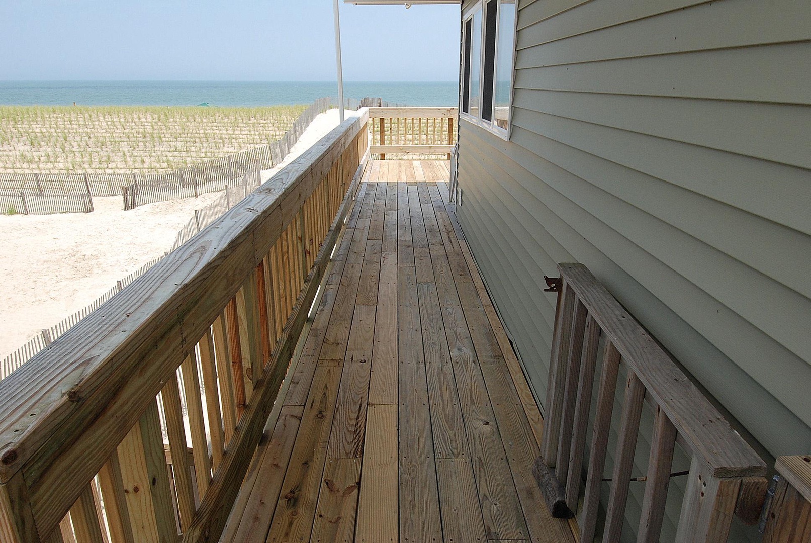 Oceanfront property featuring a wraparound deck with direct beach access. Sandy dunes and coastal fencing frame this beachside vacation rental location.